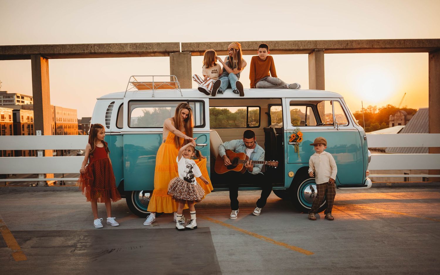 Family in and around a vintage van in a Des Moines area parking ramp at sunset during lifestyle family photo session.