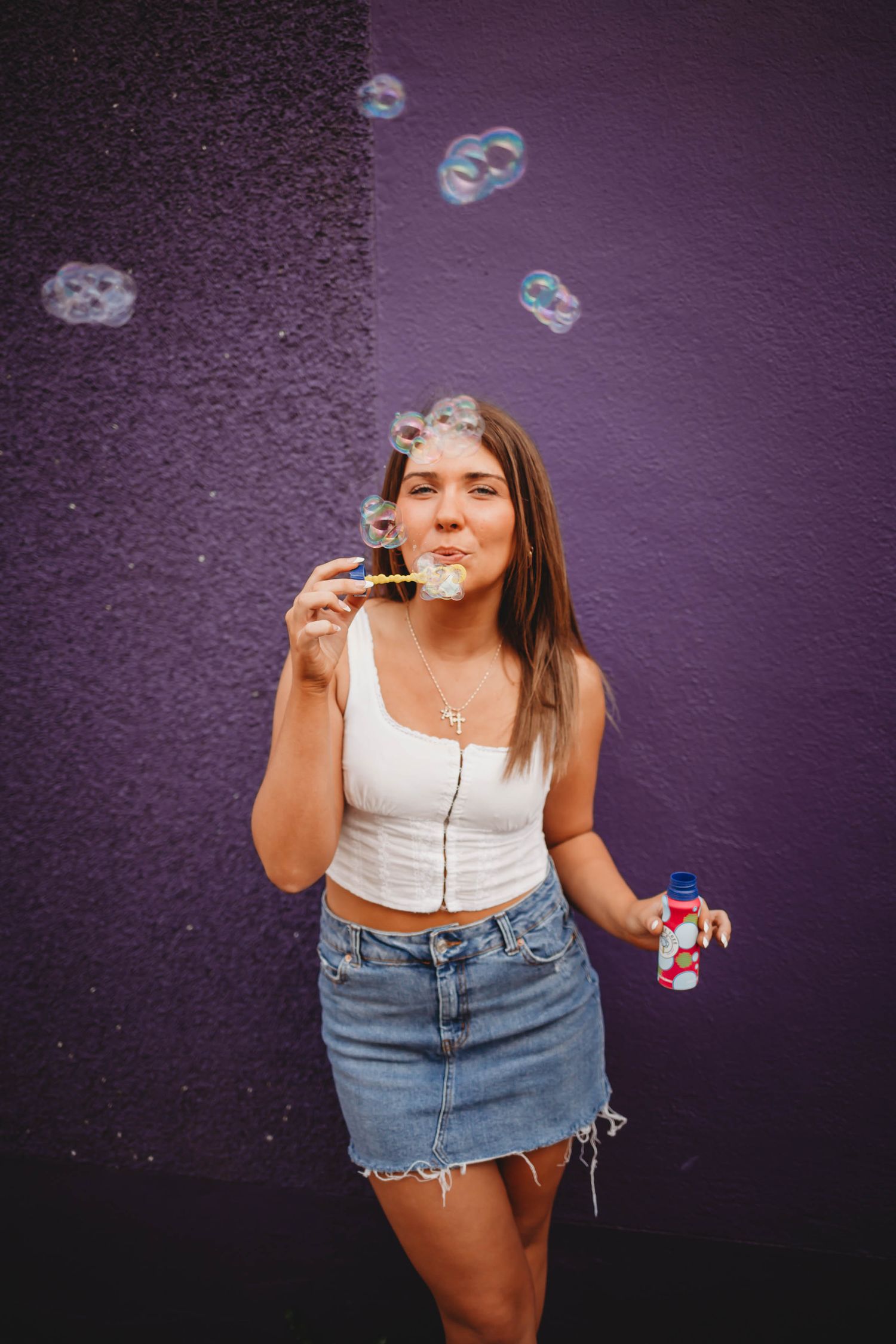 High school senior girl blows bubbles in front of a modern building in a Des Moines during a lifestyle senior photo session.