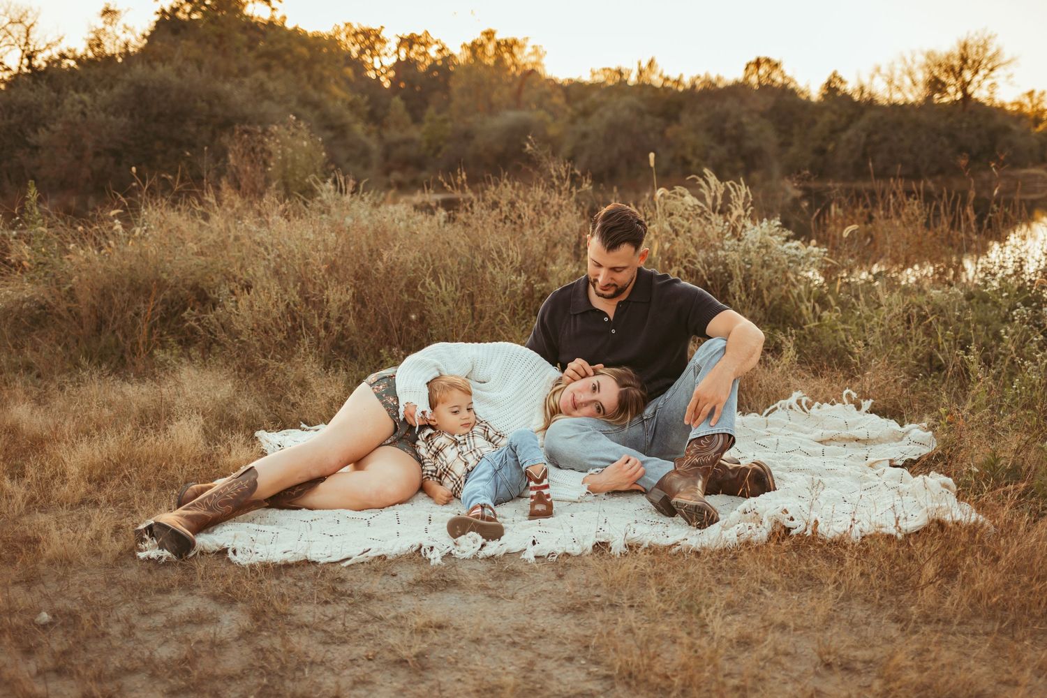 Family lays together in front of a lake in a Des Moines area park at sunset during a lifestyle family photo session.