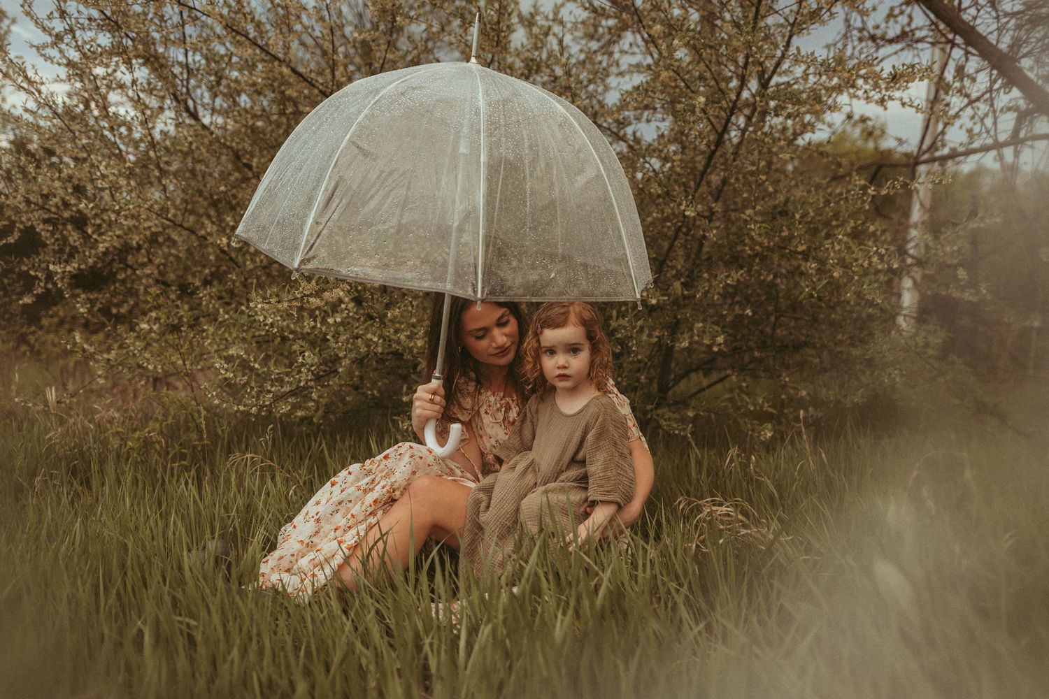 Mother and young daughter sit under an umbrella in the rain in a Des Moines area park during a lifestyle family session.