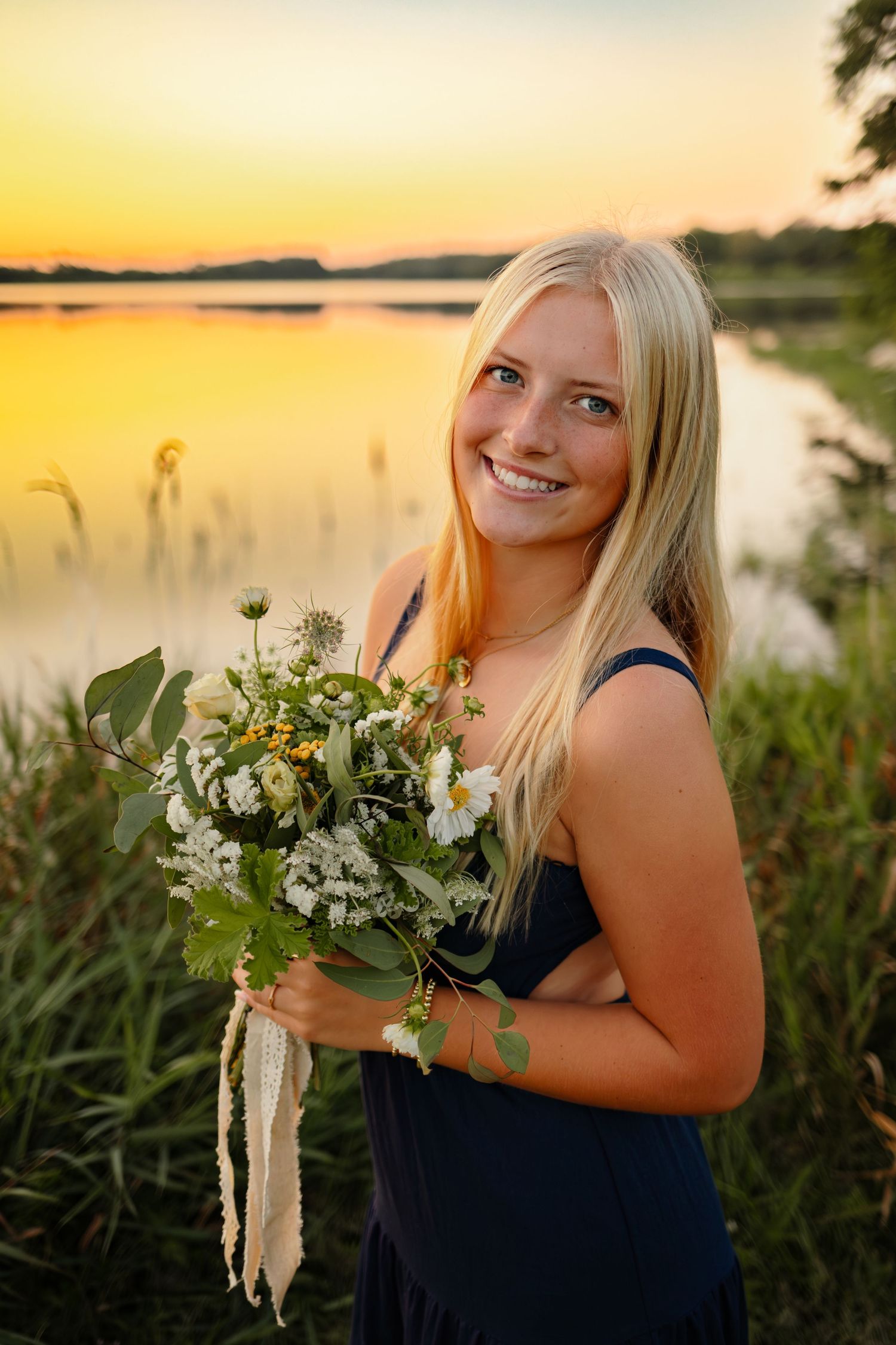 High school senior girl poses in front of a lake at sunset in a Des Moines area park during a lifestyle senior photo session.