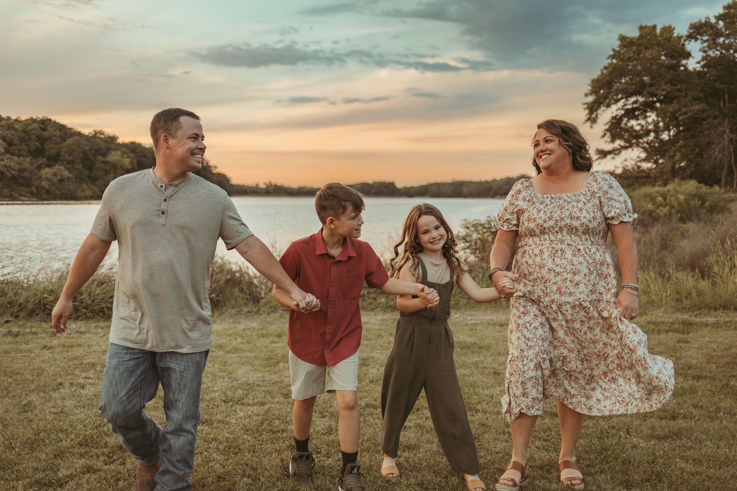 Family walks holding hands in front of a lake in a Des Moines area park at sunset during a lifestyle family photo session.