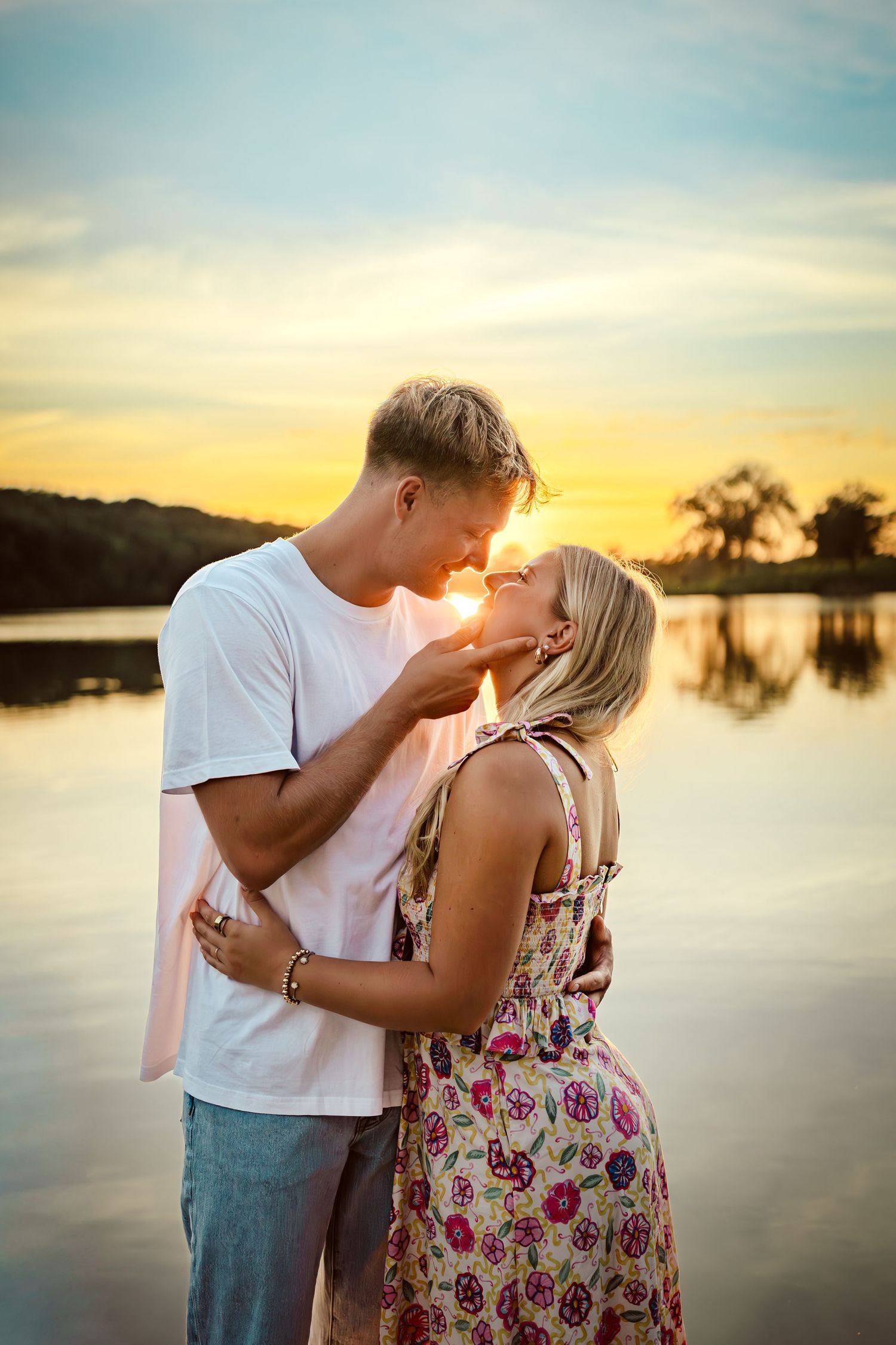 Couple hugs in front of a lake in a Des Moines area park at sunset during a lifestyle family photo session.