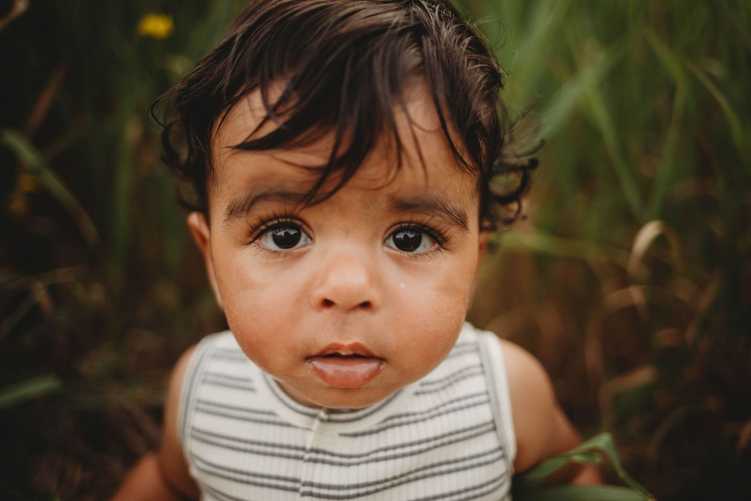 Baby boy with big eyes sits in a Des Moines area park at sunset during a lifestyle family child milestone photo session.