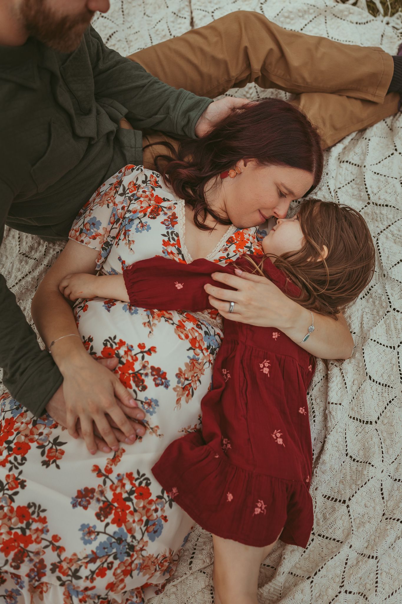Mother snuggles daughter while laying on a vintage blanket  at sunset in a Des Moines area park during a lifestyle family photo session.