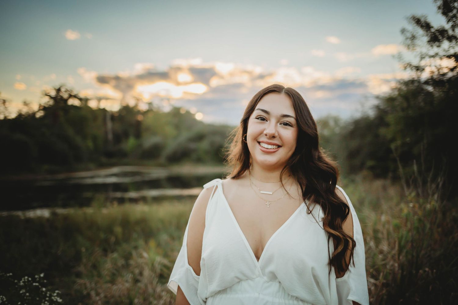 High school senior girl poses in front of a lake in a Des Moines area park at sunset during a lifestyle senior photo session.
