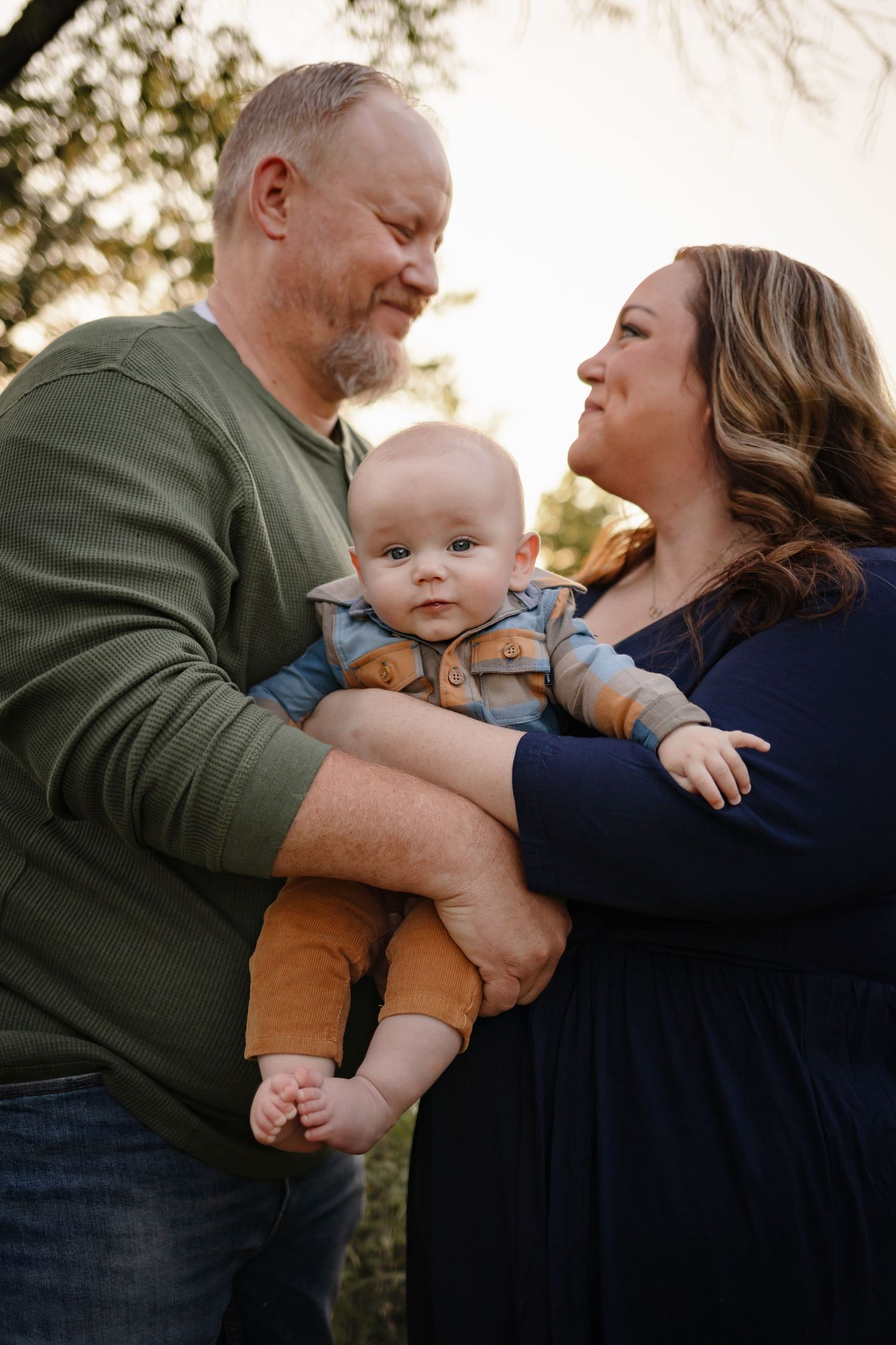 Mother and father hold young baby boy in a Des Moines area park at sunset during a lifestyle family photo session.