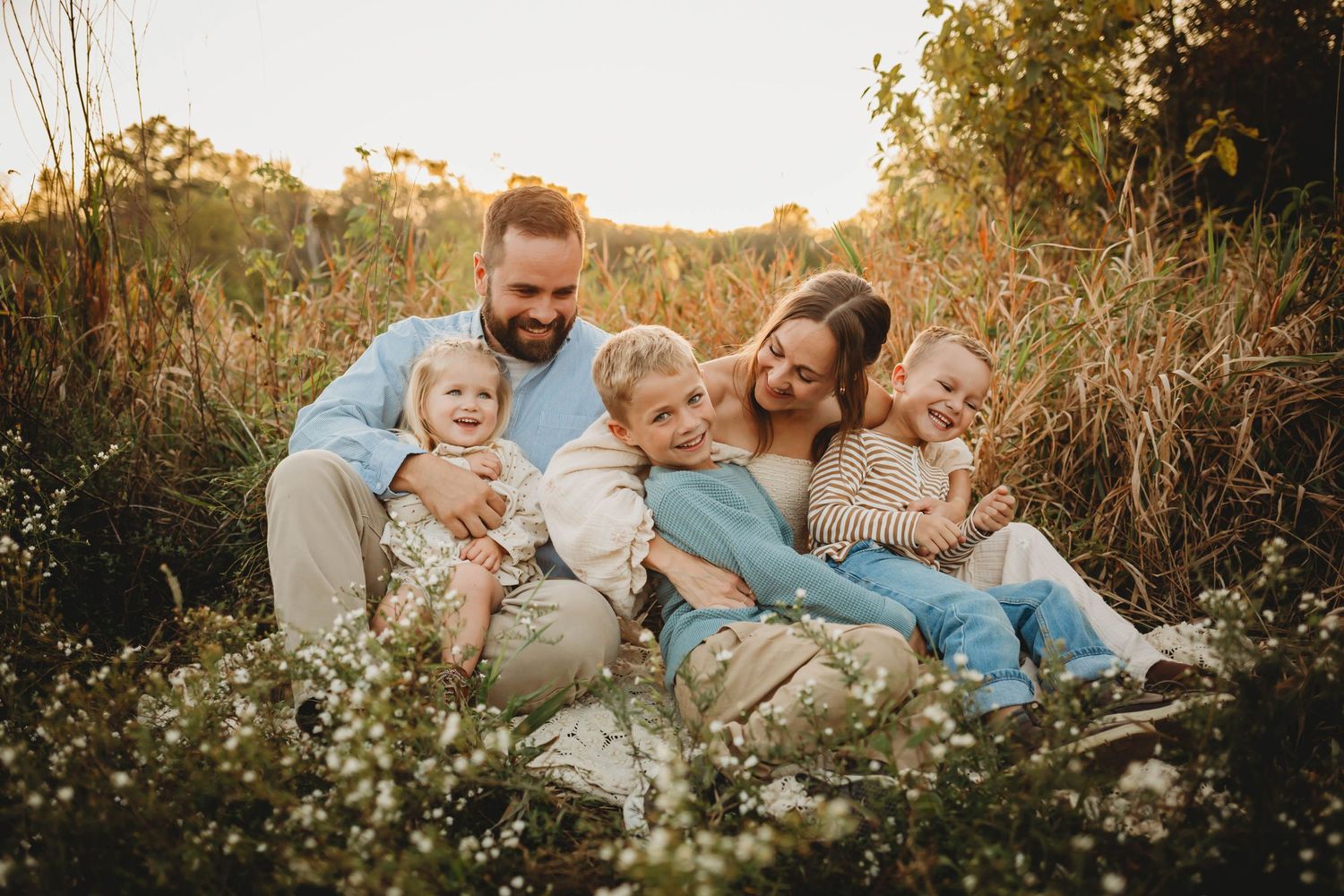 Family sits among flowers in a Des Moines area park at sunset during a lifestyle family photo session.