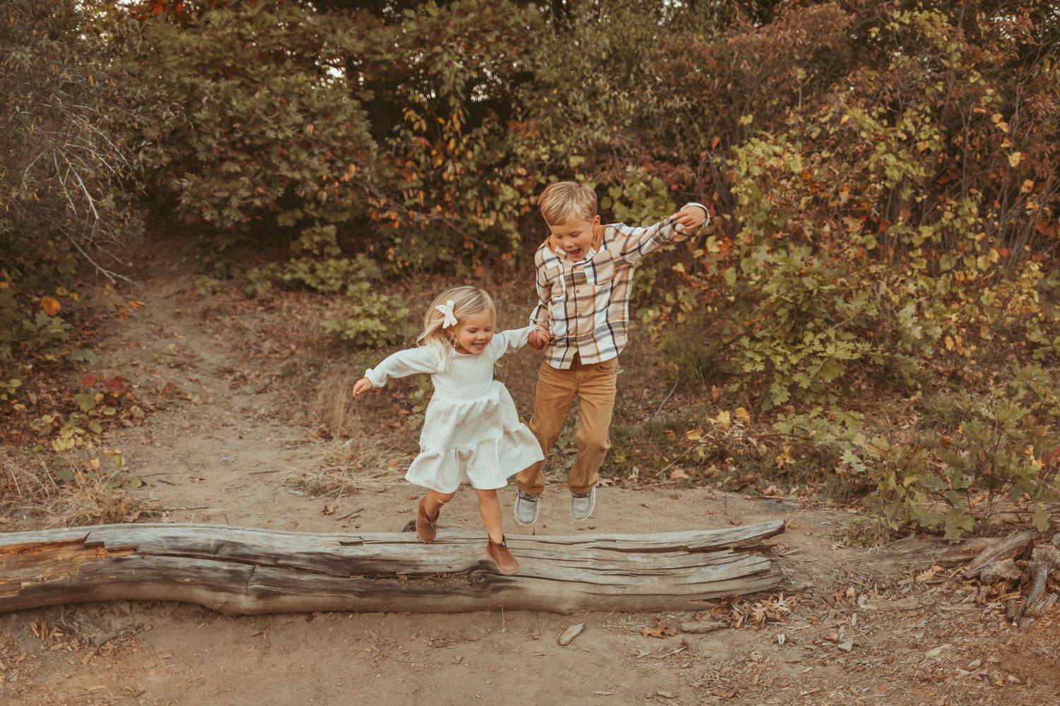 Brother and sister jump off log in a Des Moines area park at sunset during a lifestyle family child milestone photo session.