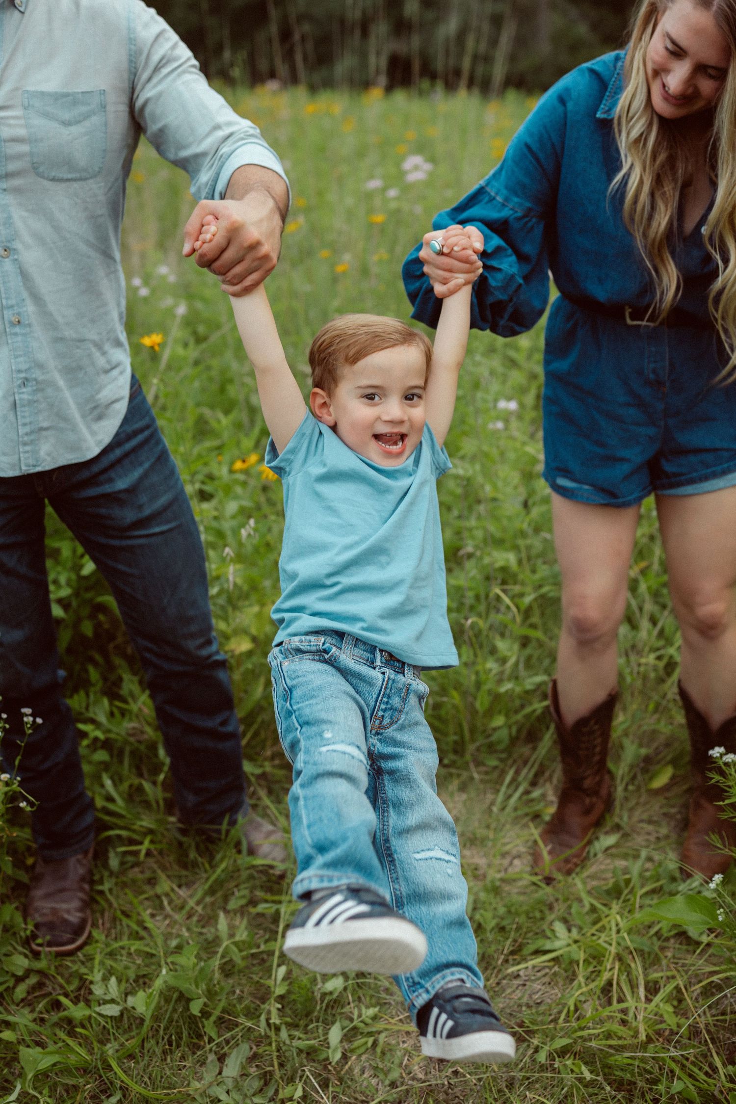Parents swing little boy in a Des Moines area park at sunset during a lifestyle family photo session.