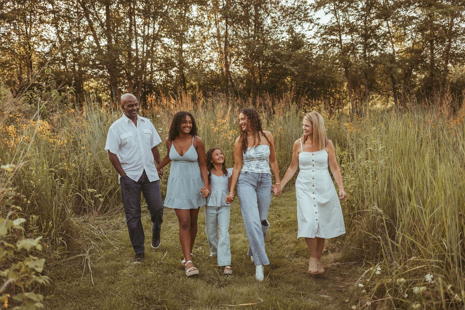 Family holds hands and walk in a field in a Des Moines area park at sunset during a lifestyle family photo session.