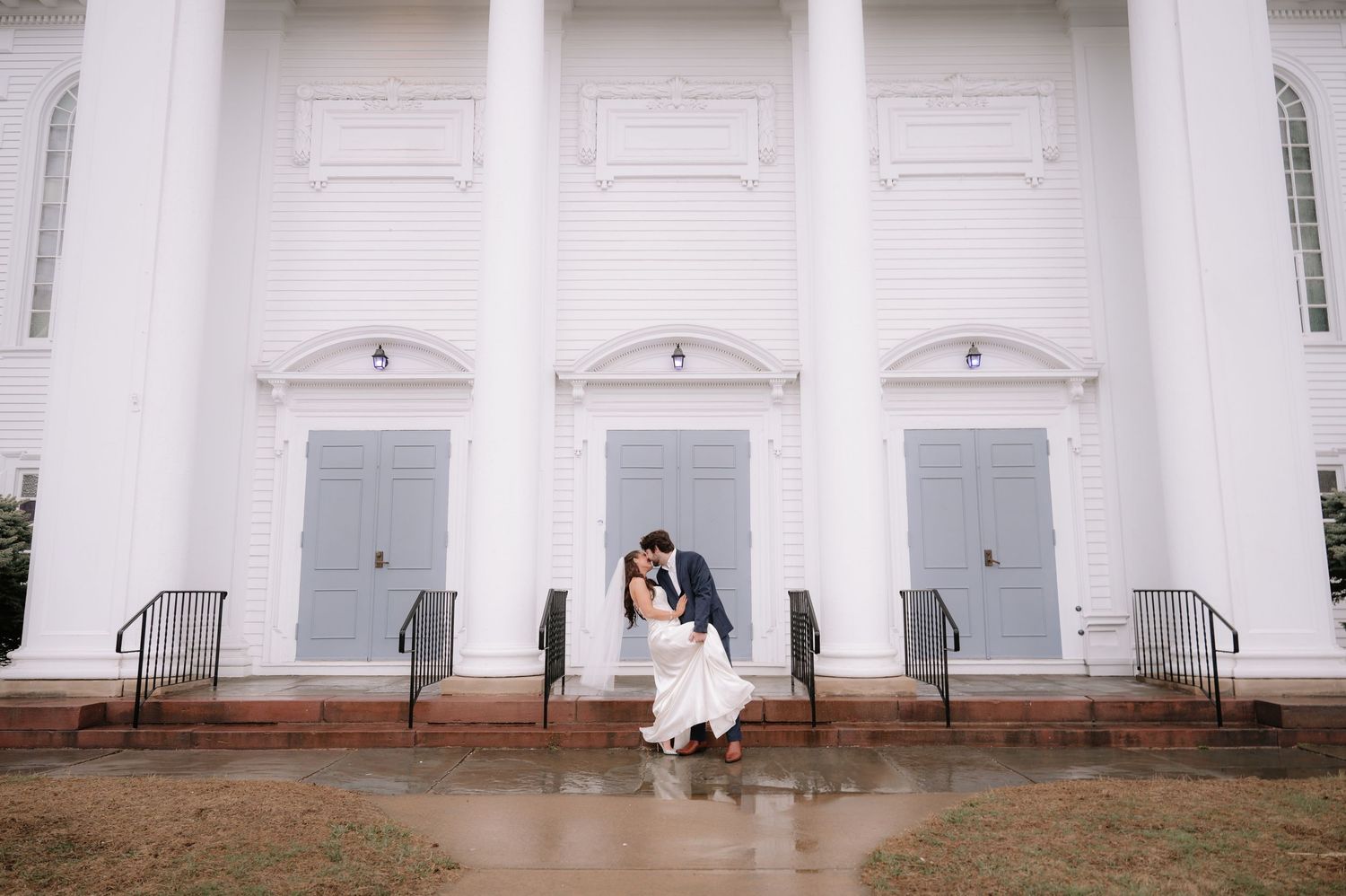 Wedding couple sits on steps of white columned building with grand architecture.