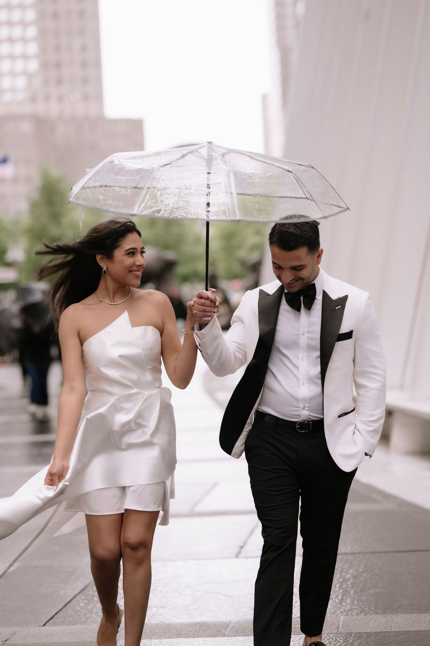 Stylish couple walking under clear umbrella in urban setting.