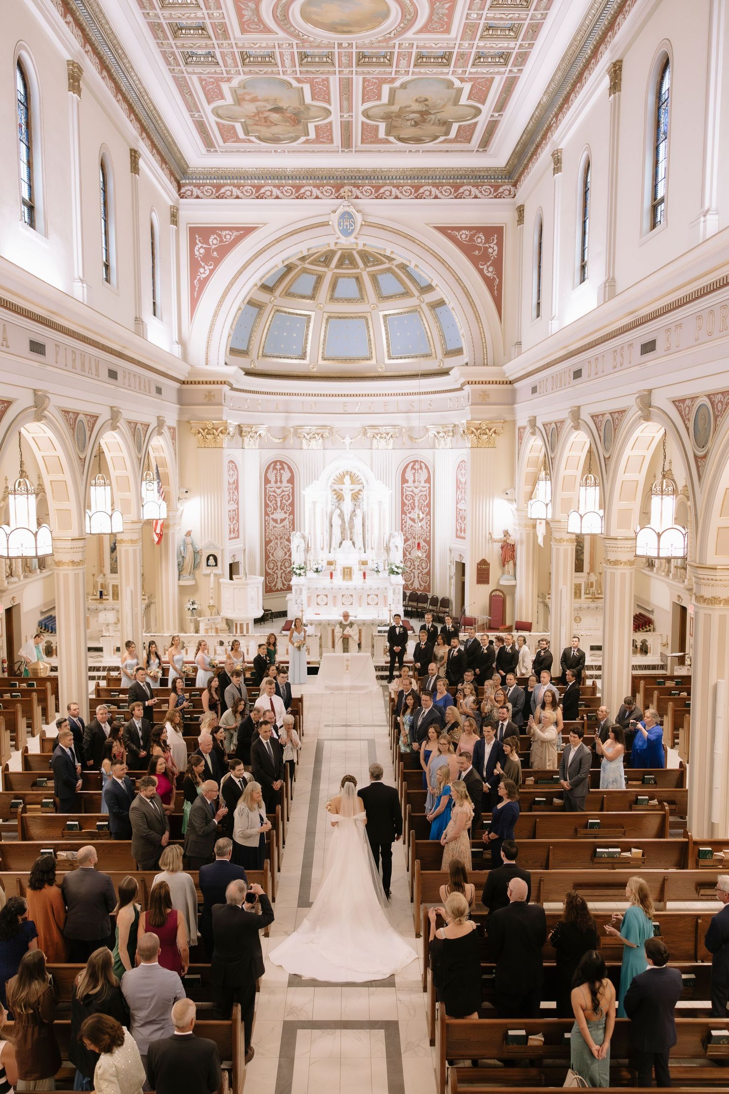High-angle view of a traditional Catholic church wedding ceremony with ornate architecture and guests filling wooden pews.