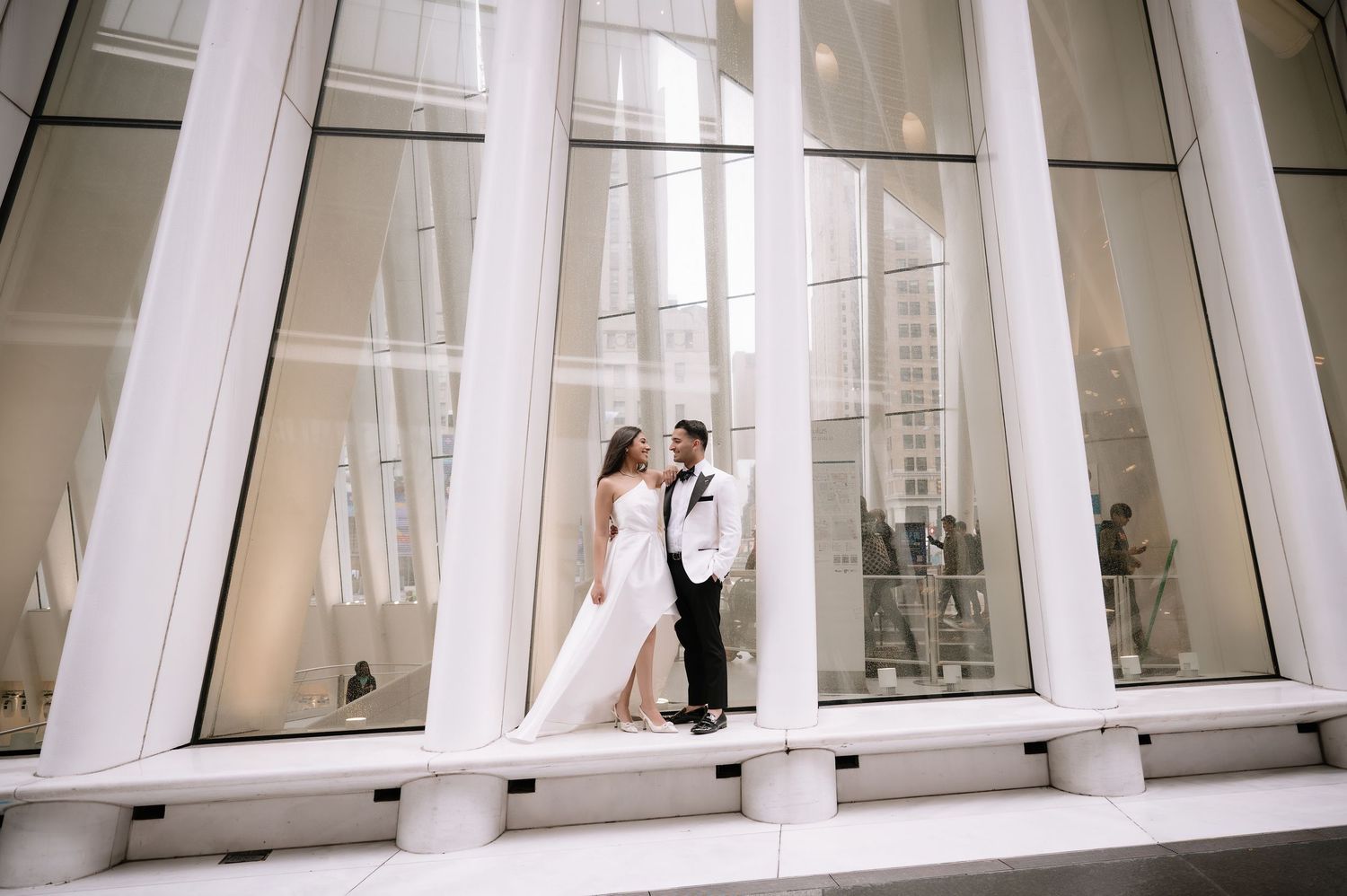 Wedding couple embracing in modern architecture with floor-to-ceiling windows and city views.
