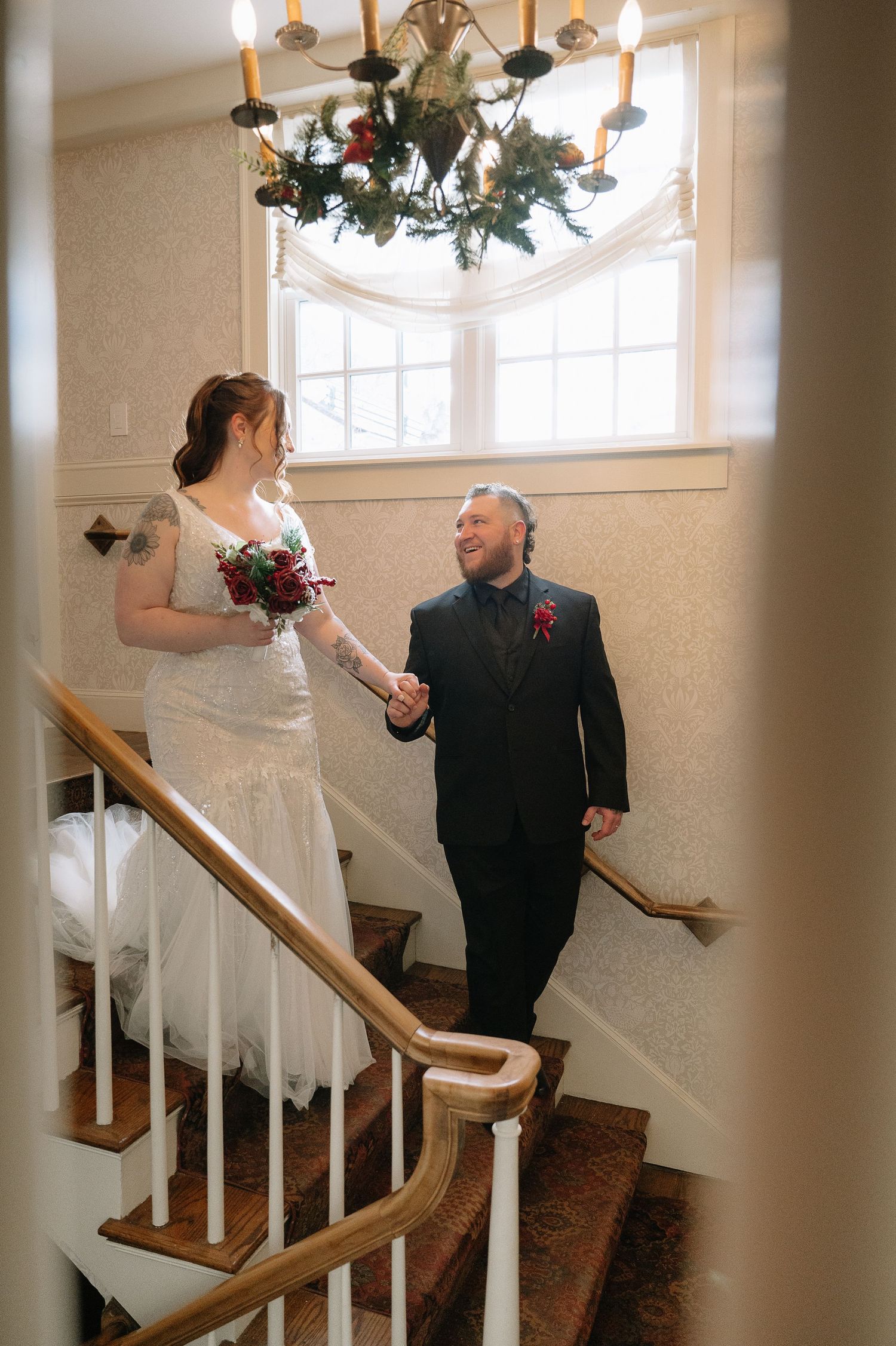 A wedding couple shares a joyful moment on an elegant staircase under a chandelier.