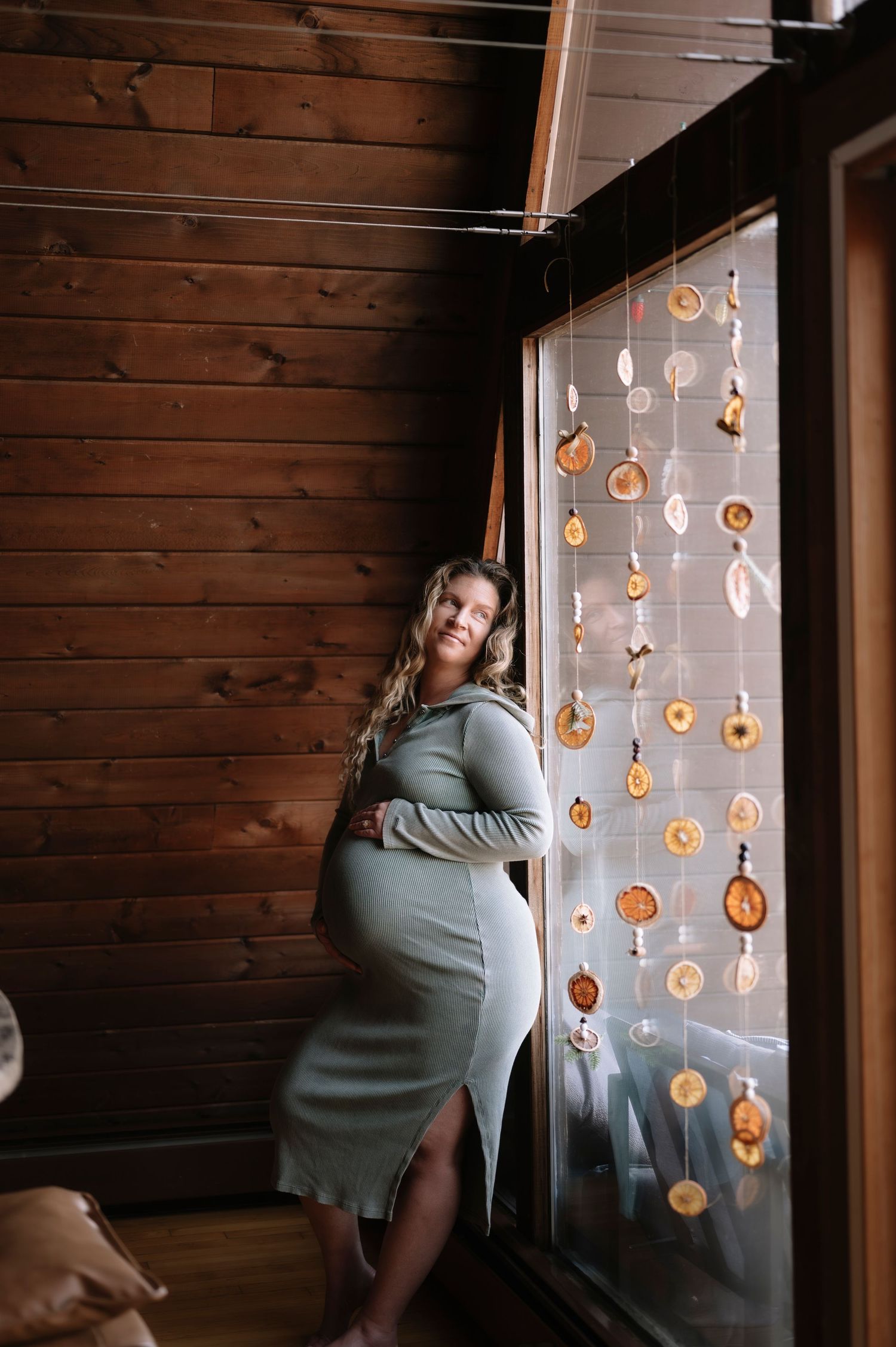 A series of photos showing a person in a gray dress posing near a window with decorative hanging ornaments.