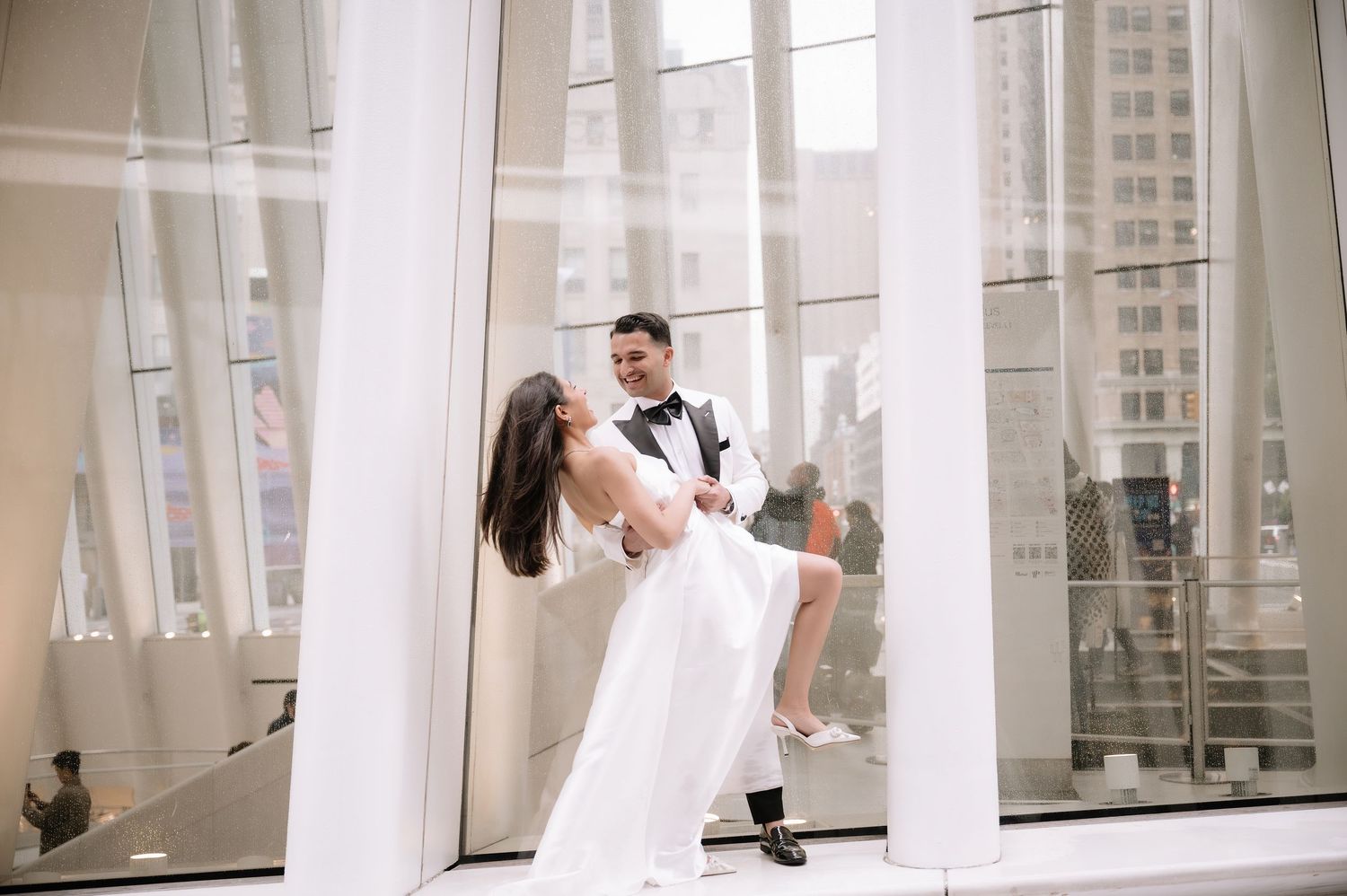 Couple in wedding attire performing romantic dance dip between white columns.