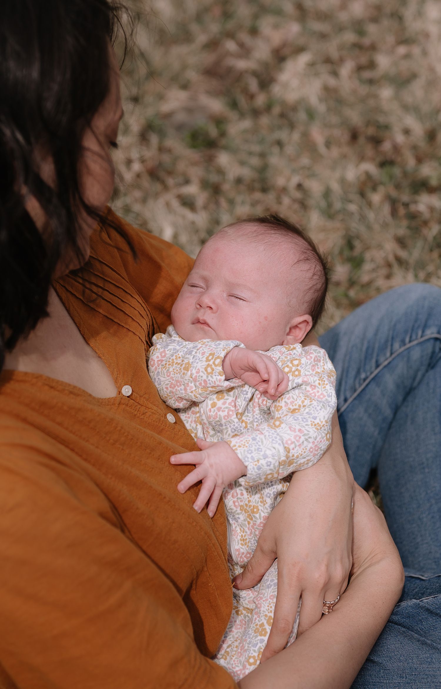 A sleeping baby in floral clothing rests peacefully against an orange sweater.