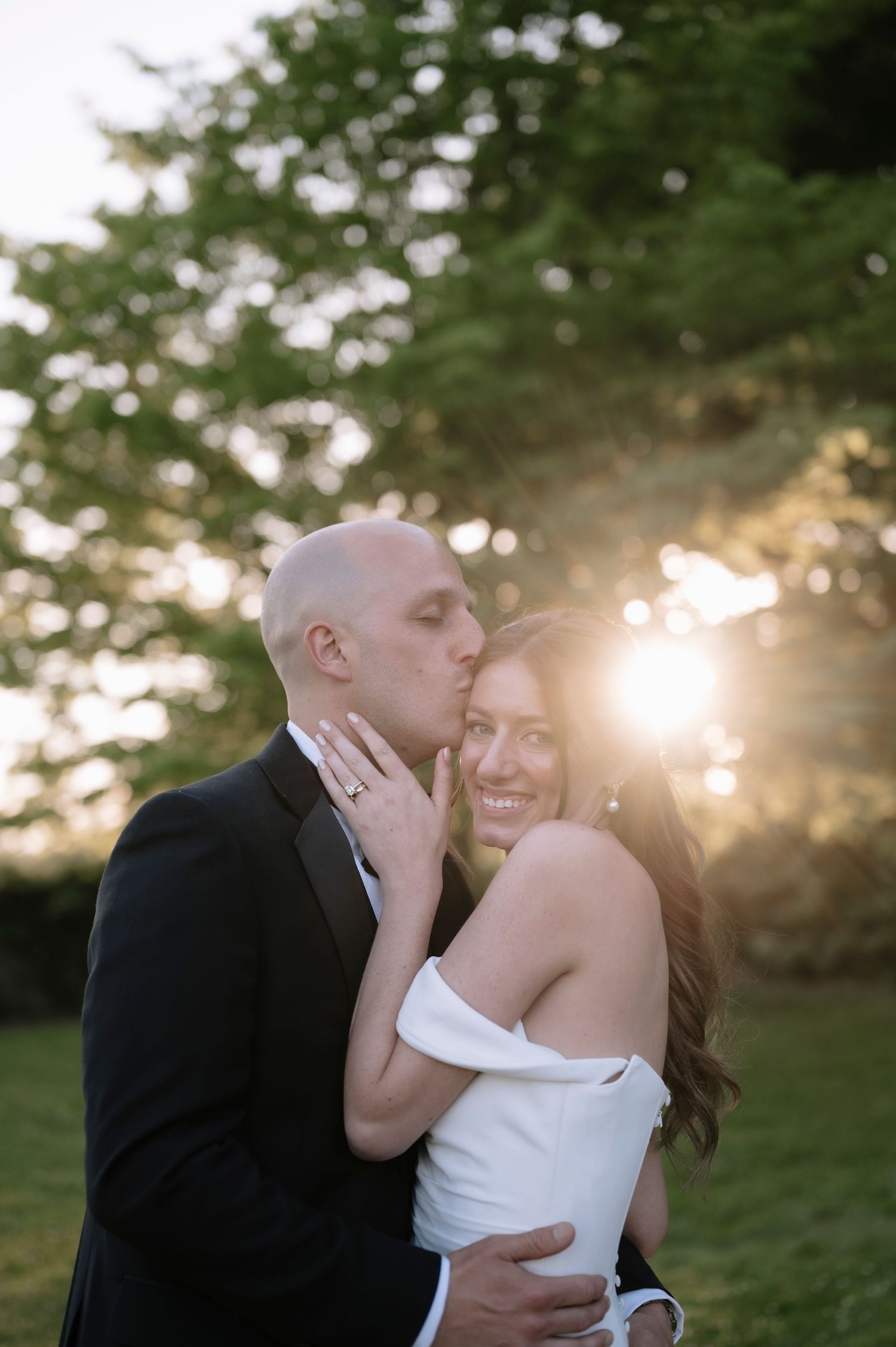 A romantic wedding couple embraces during golden hour sunset in a lush outdoor garden setting.