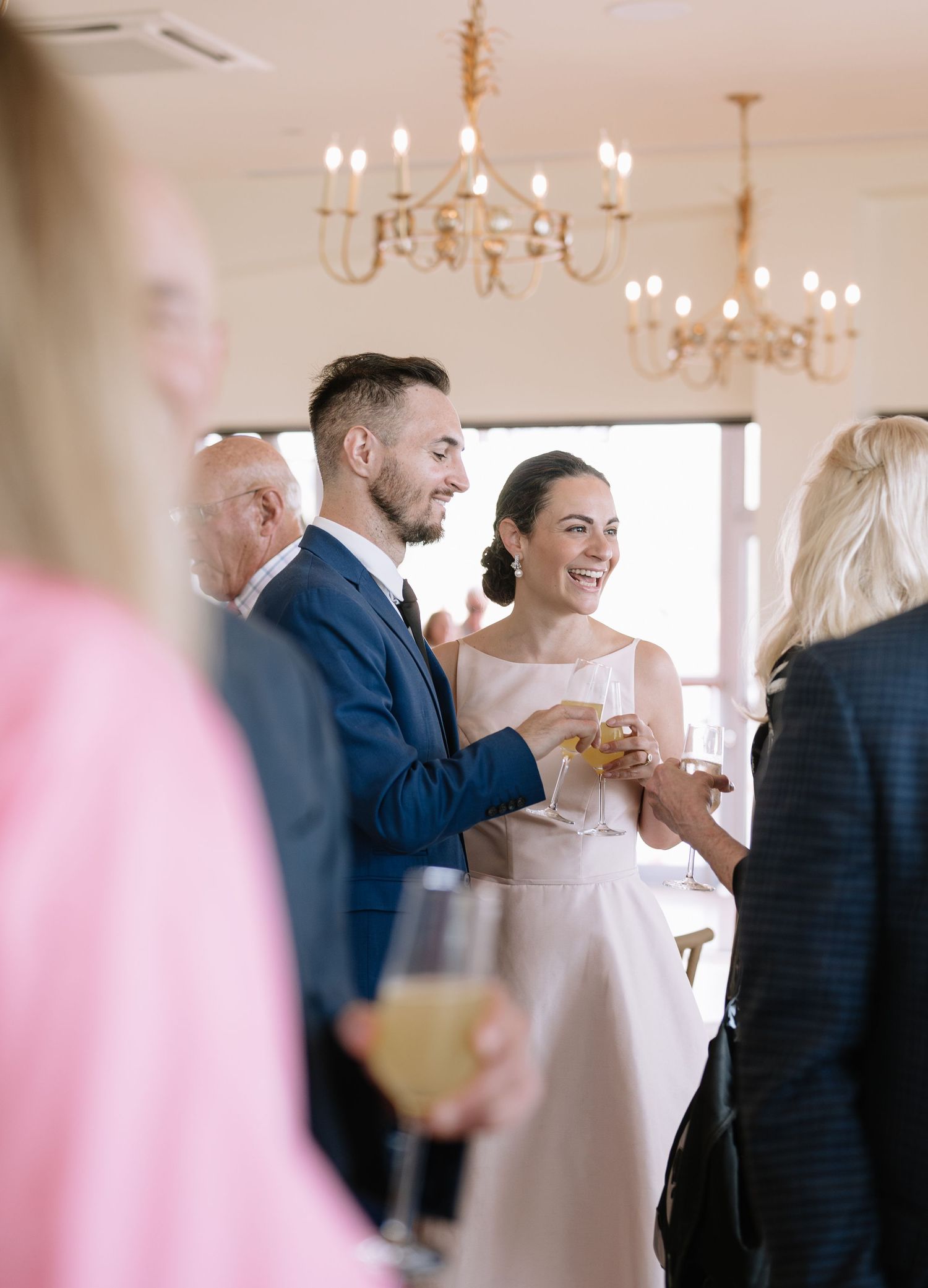 Guests mingle and socialize during an elegant reception in a bright room with crystal chandeliers.