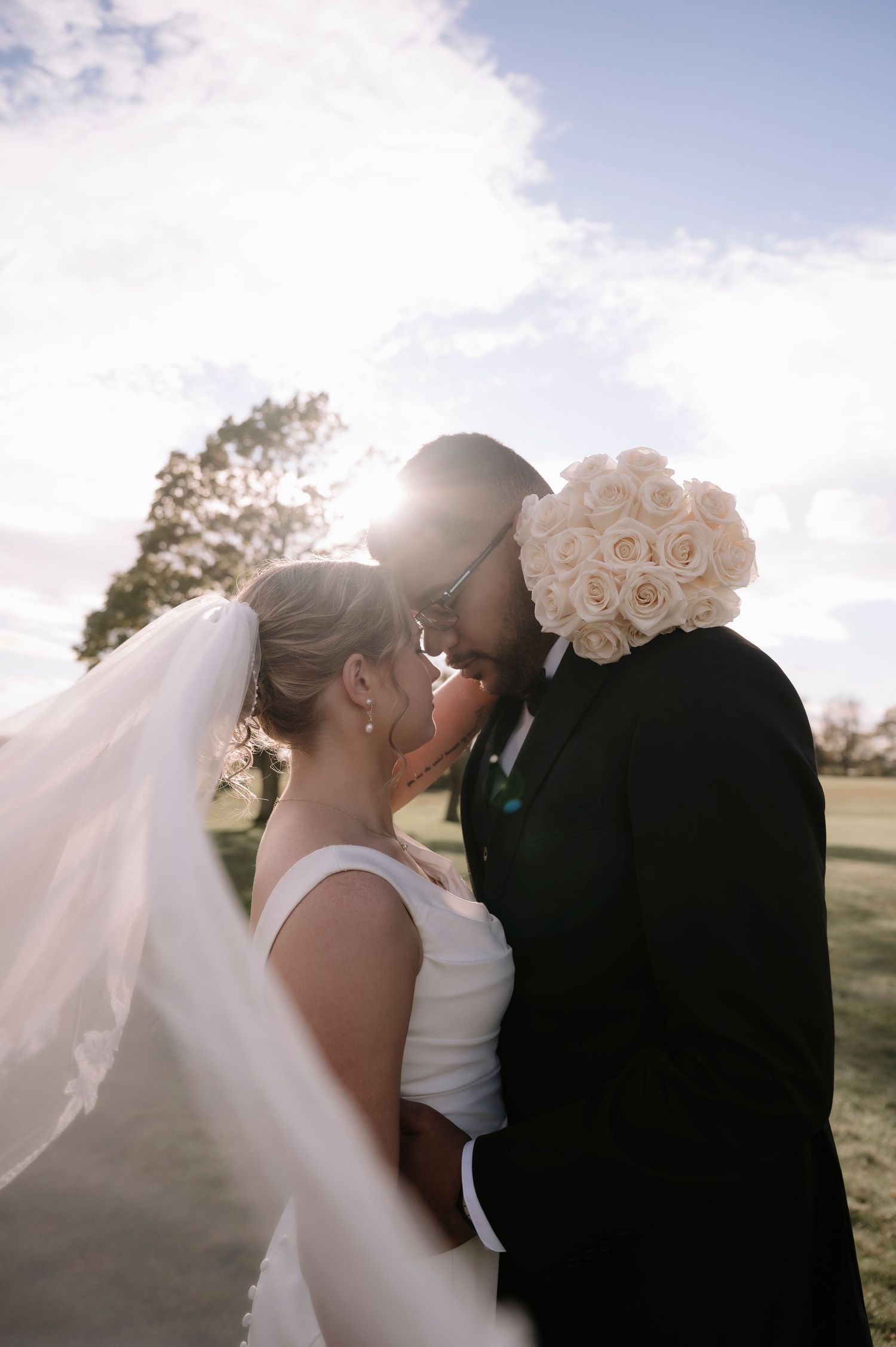 A romantic wedding moment captured at sunset with soft lighting and flowing white veil in the breeze.