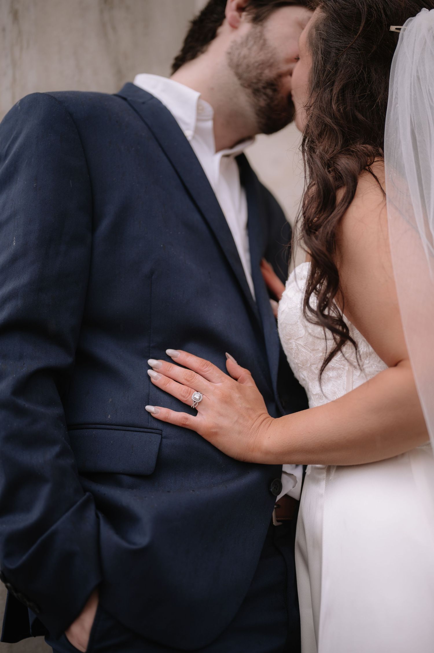 Close-up of couple embracing, showing detailed lace wedding dress and navy suit.