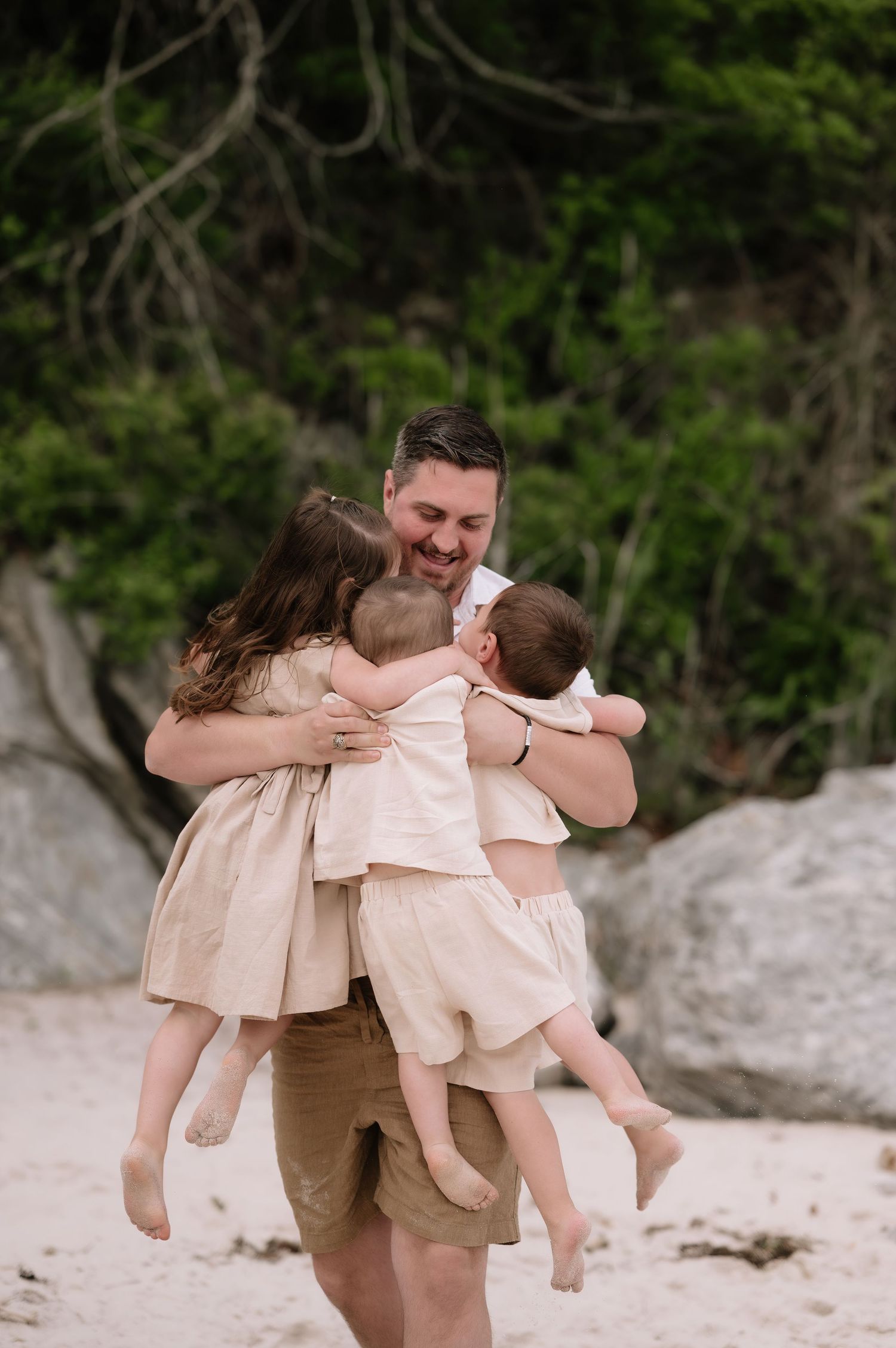 A joyful family embrace on a sandy beach with lush greenery in the background.