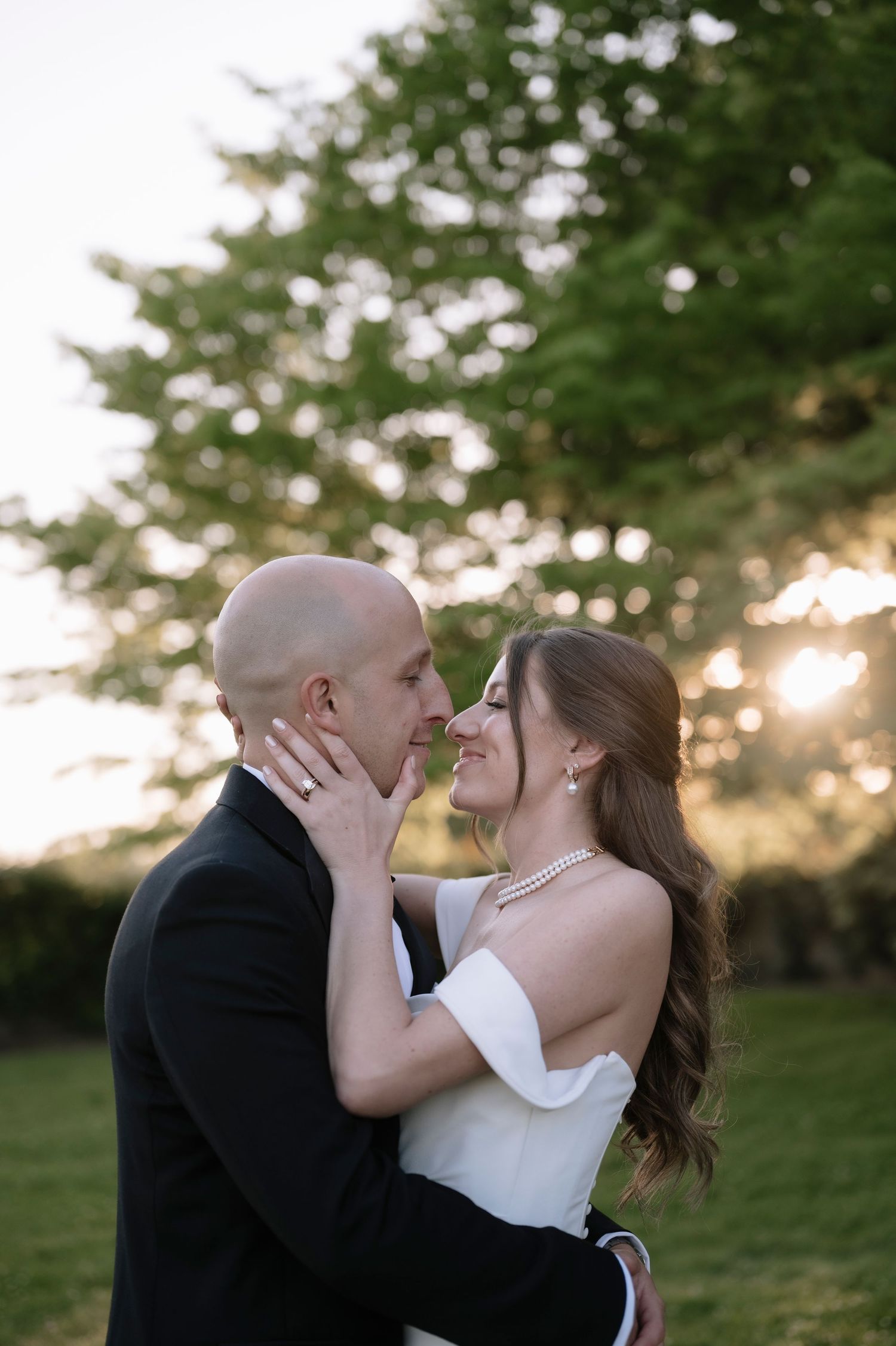 Romantic couple embraces in a sunset garden setting with trees silhouetted in the background.