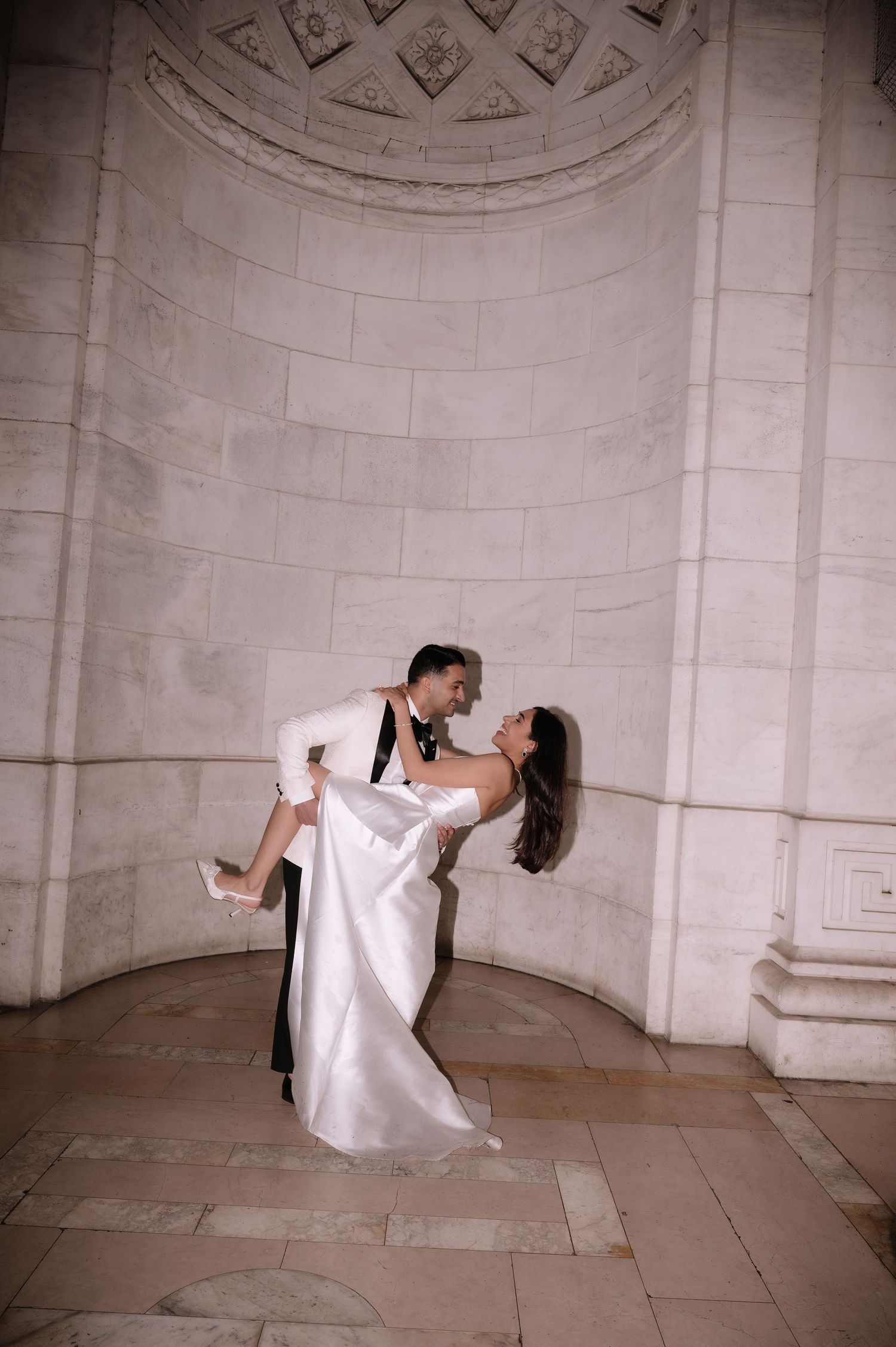 A couple in wedding attire performs a romantic dip pose in a grand marble archway.