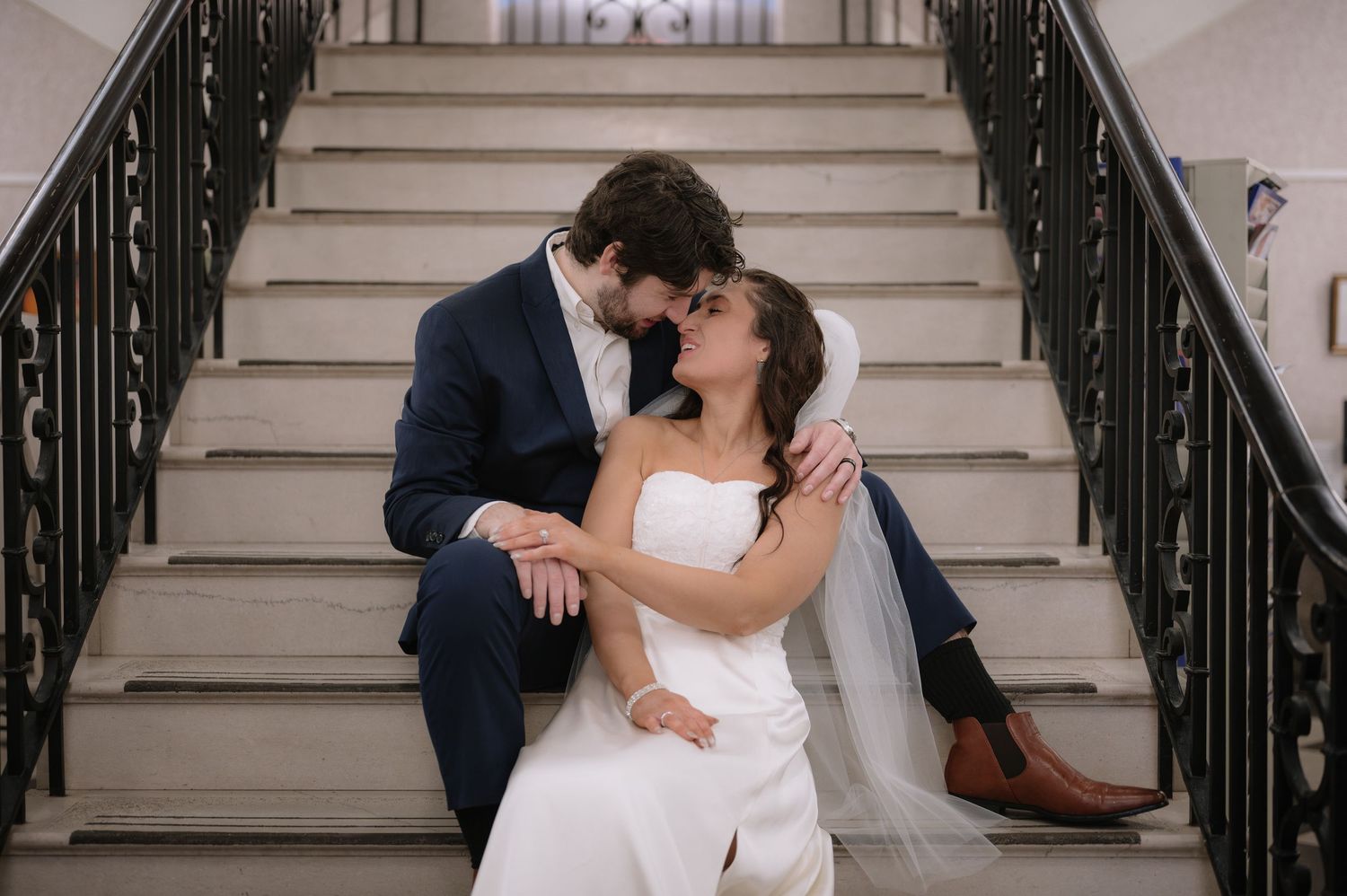 Intimate moment between couple on elegant white staircase with decorative black railings.
