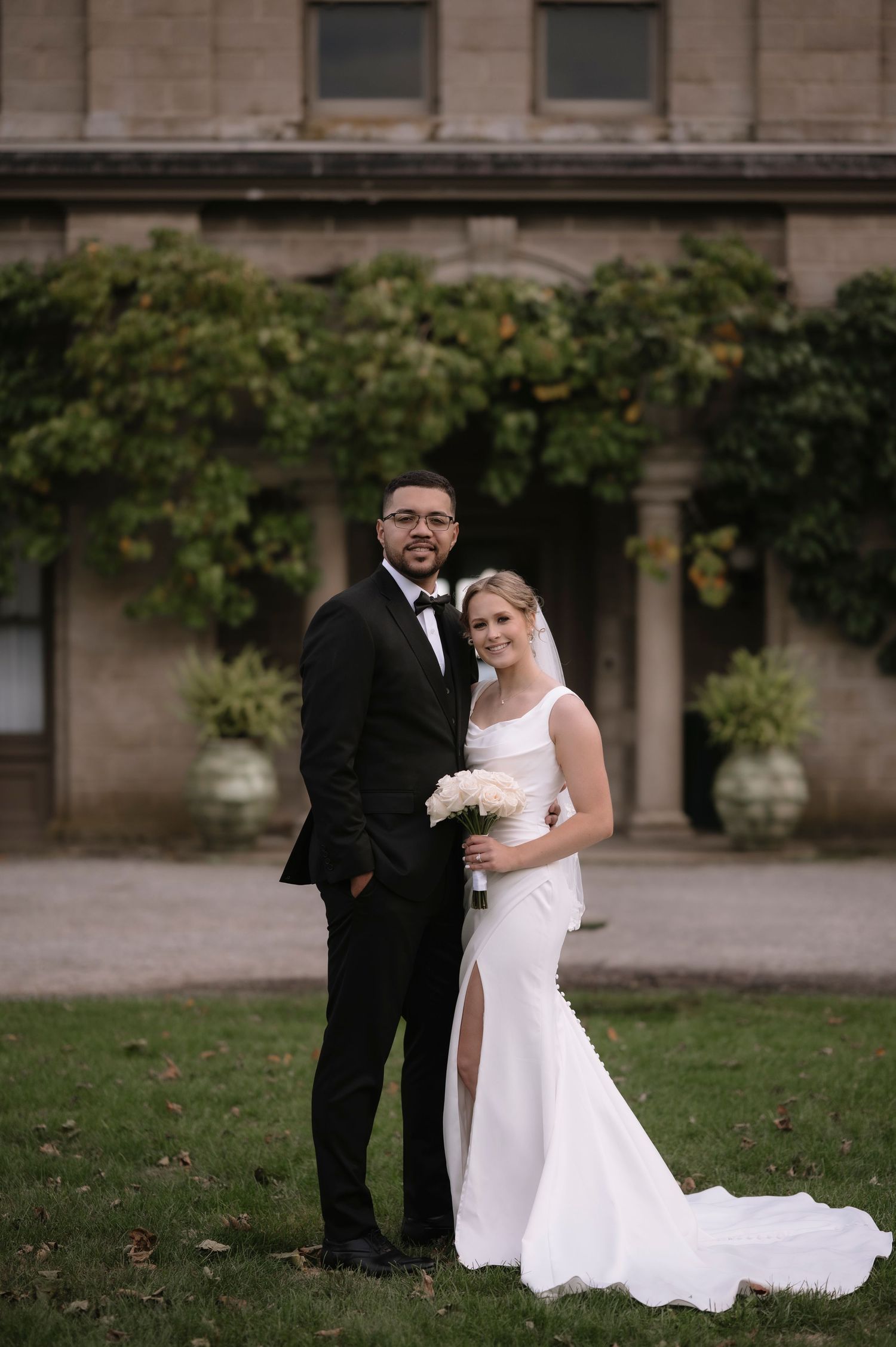 Wedding couple poses for romantic portraits in front of a historic stone building with trailing vines.