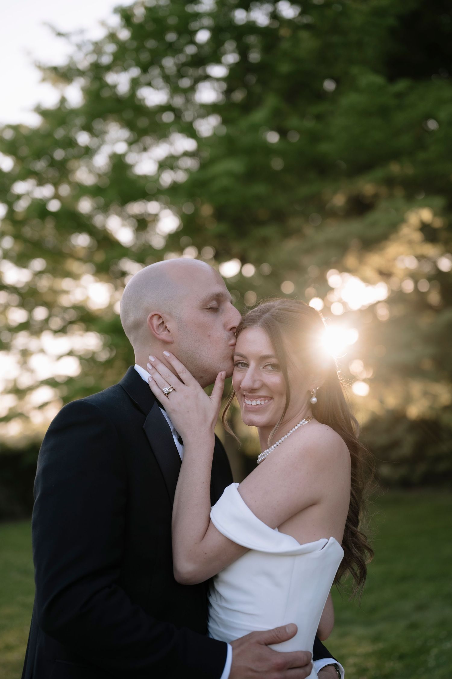 A romantic couple embraces during sunset in a garden setting with soft golden light filtering through trees.
