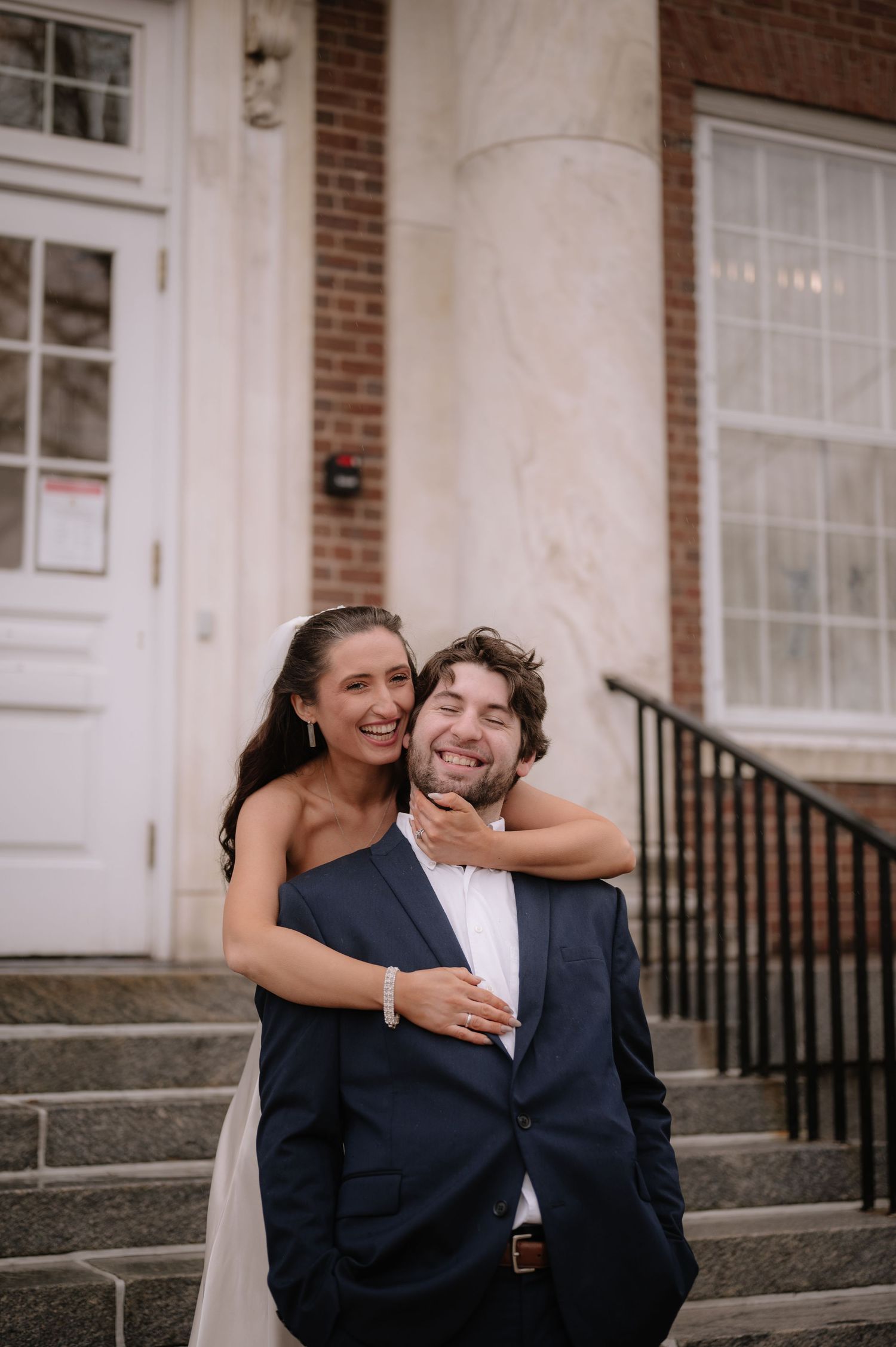 Couple sharing playful embrace on building steps with brick and white columns.