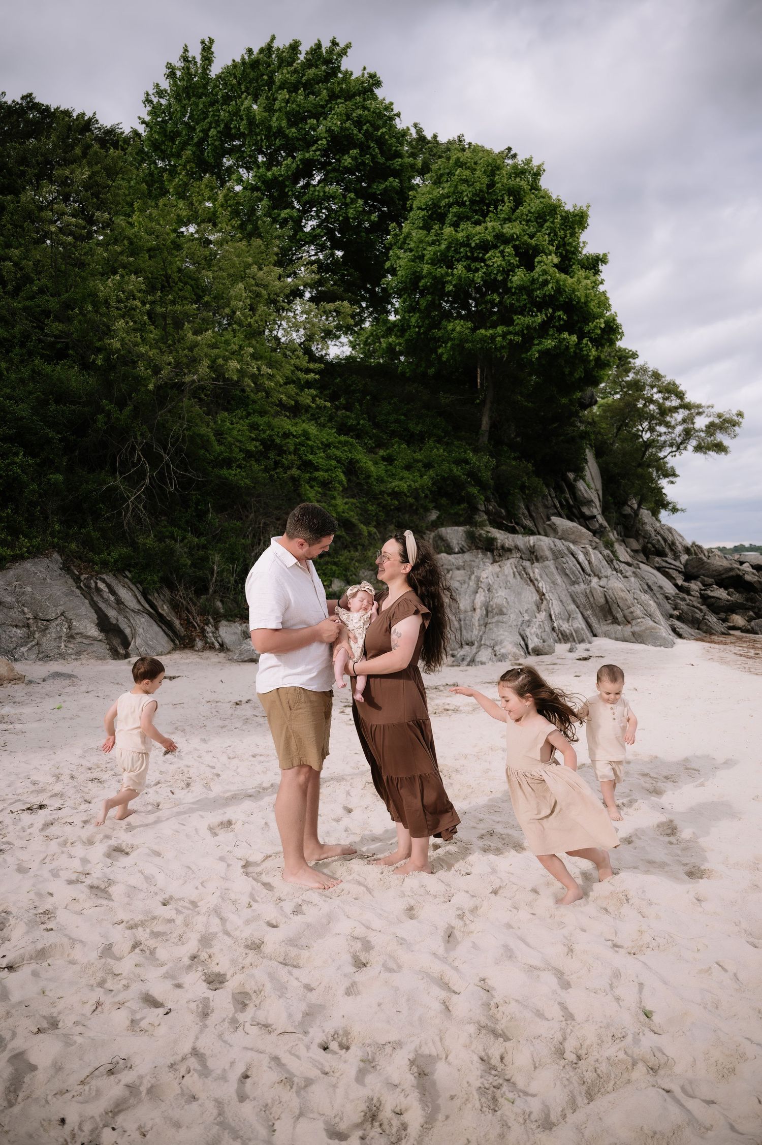 Family enjoying a beach day near rocky cliffs and trees on a sandy shoreline.