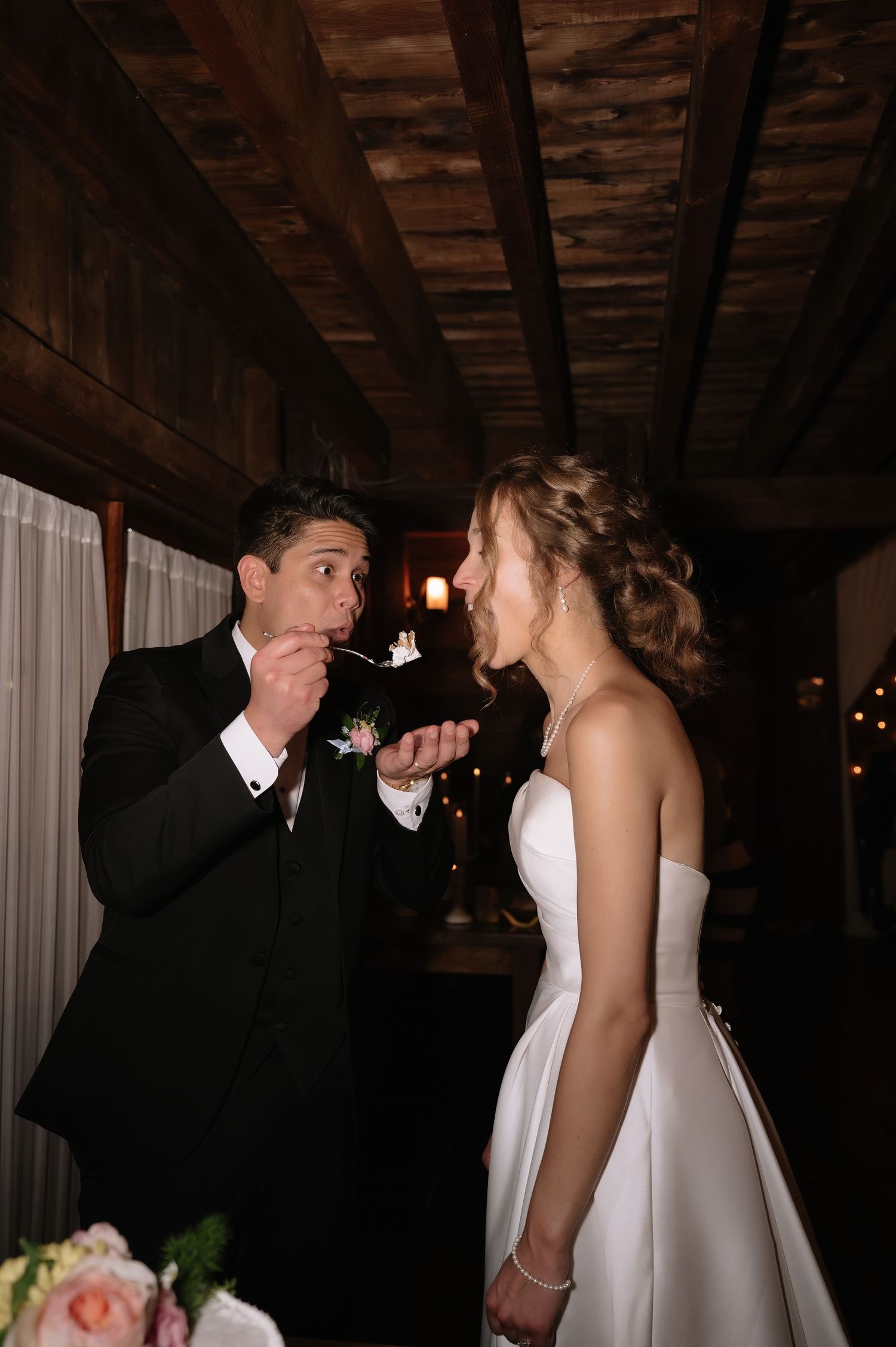 Bride and groom share a sweet cake tasting moment at their wedding reception in a rustic venue.