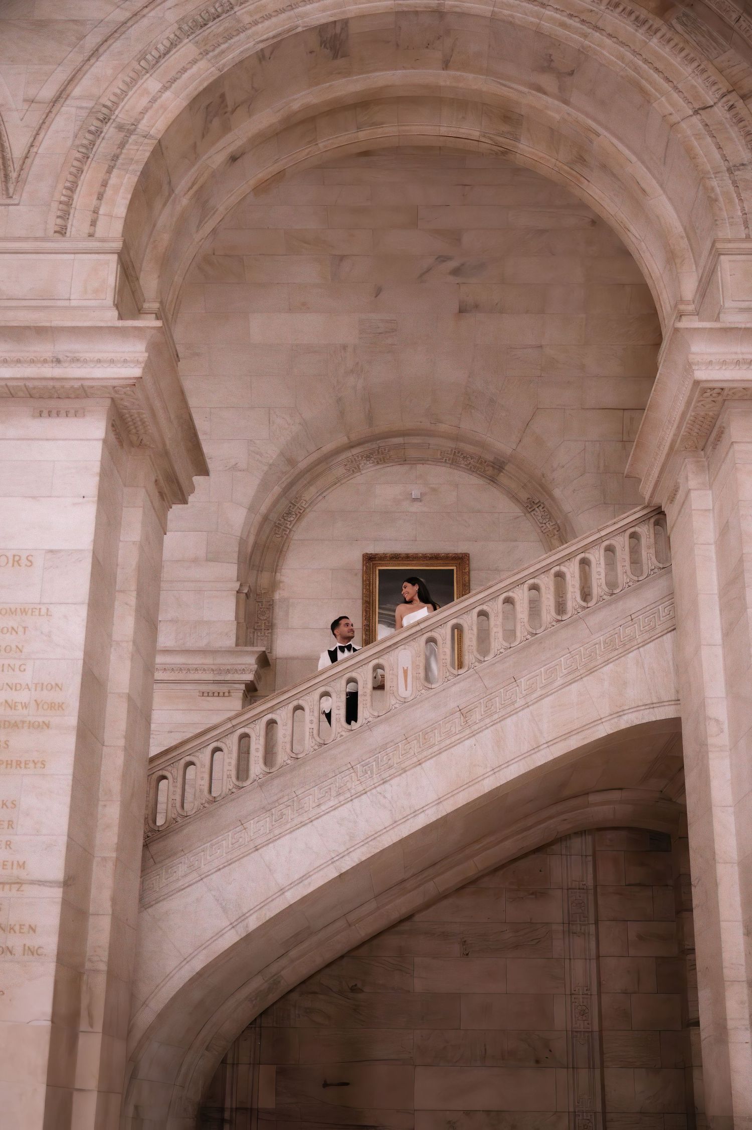 A couple in wedding attire standing on an elegant curved marble staircase.