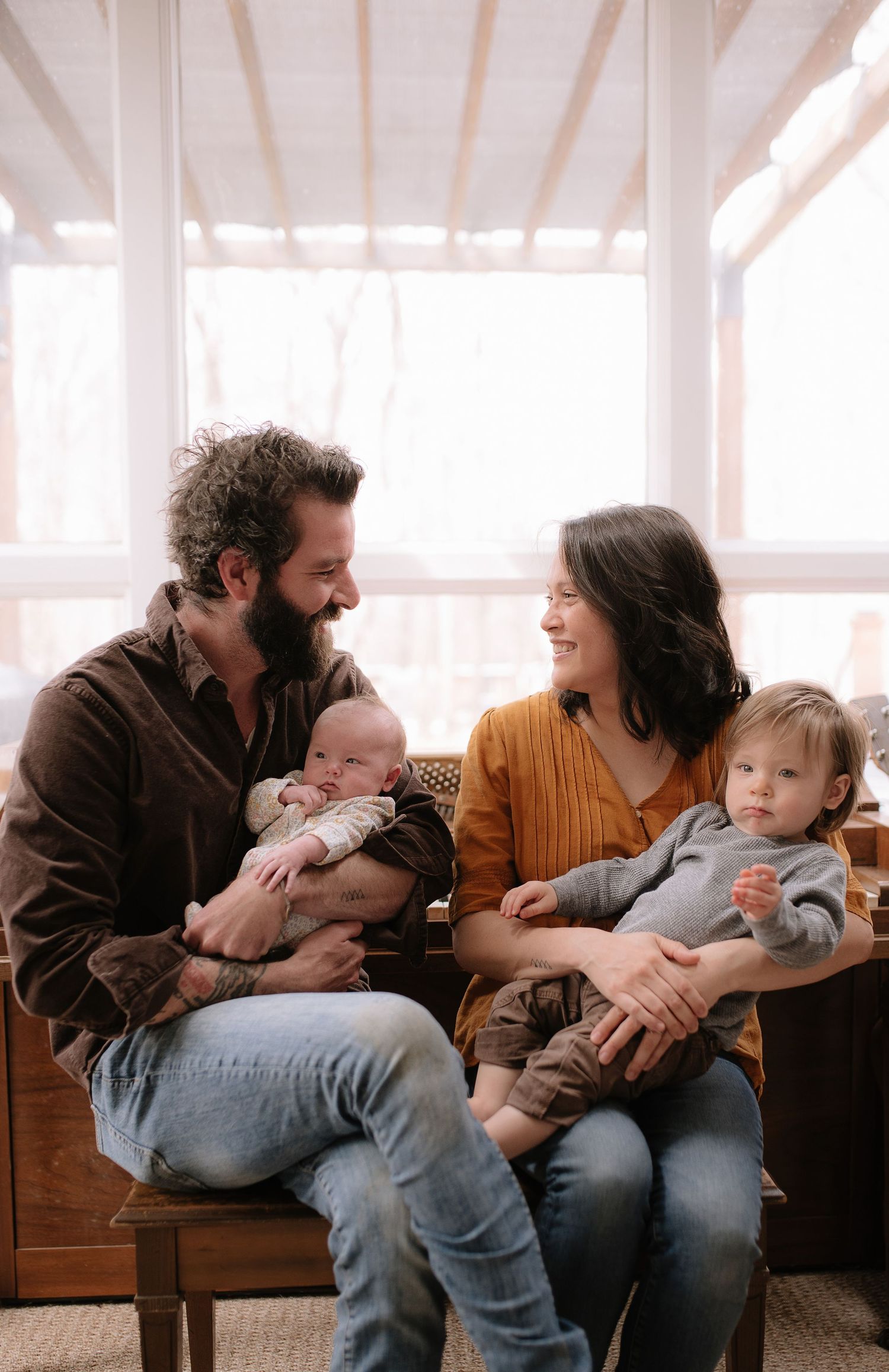 Family of four sitting together on wooden bench in sunlit room.