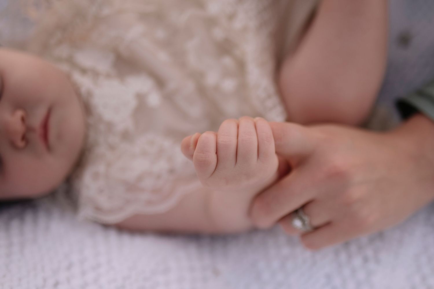 A tiny hand grasps an adult hand while resting on white fabric.
