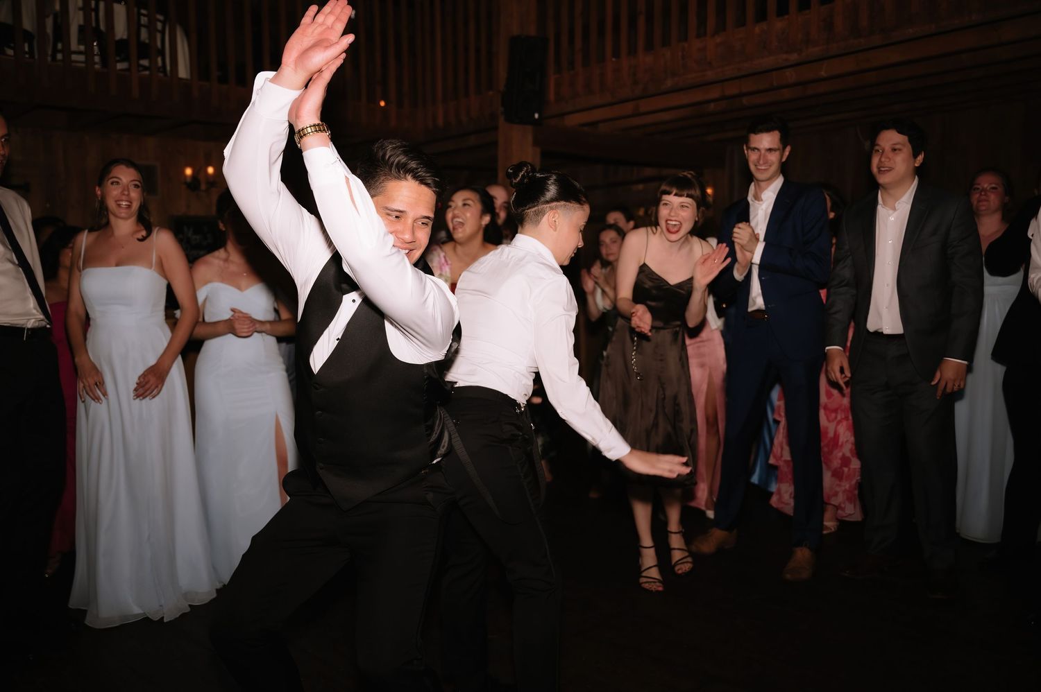 Two men dancing energetically at a wedding reception while guests clap and celebrate in the background.