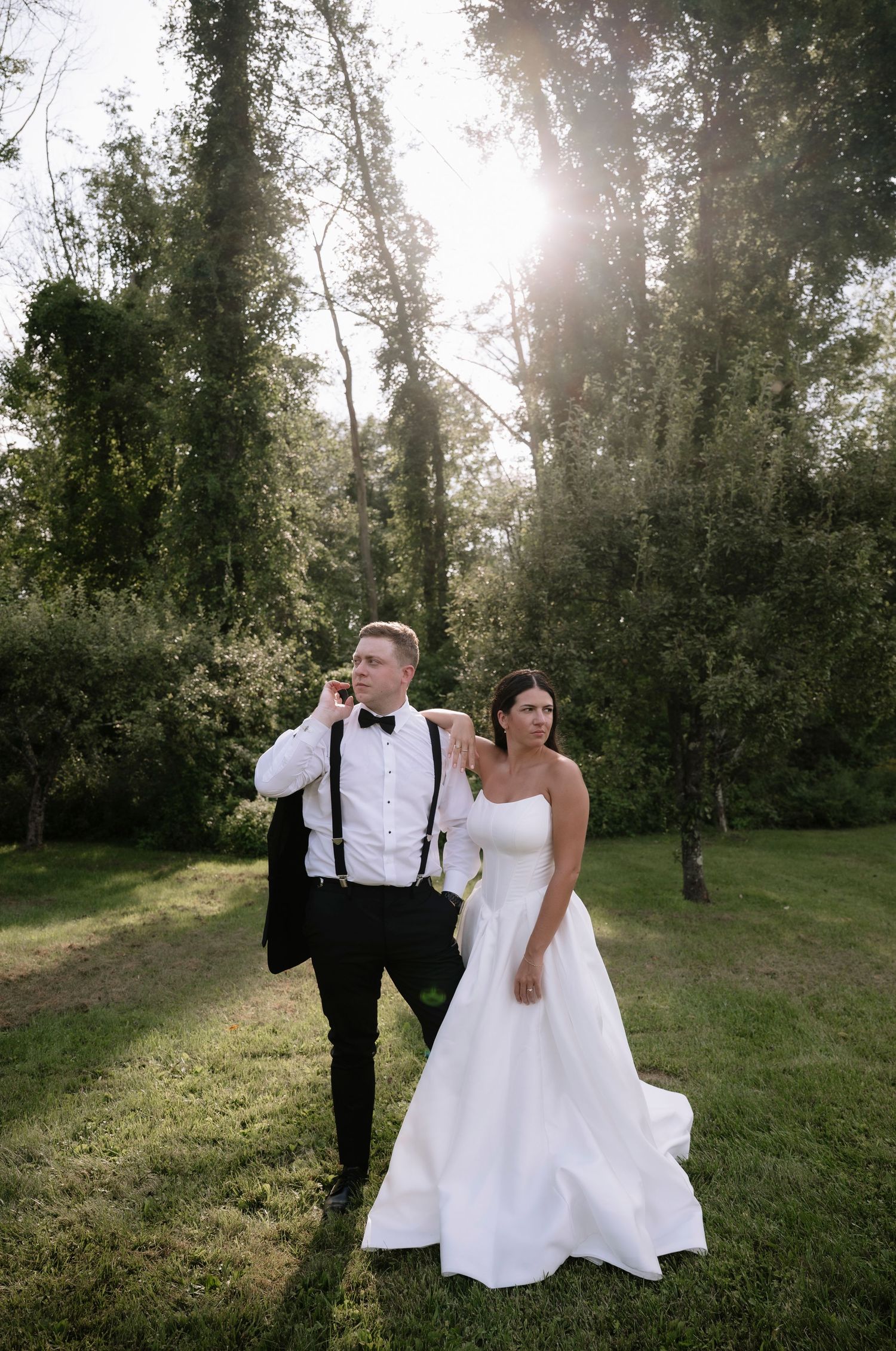 Wedding couple shares a playful moment drinking beverages together in a sunlit forest setting.