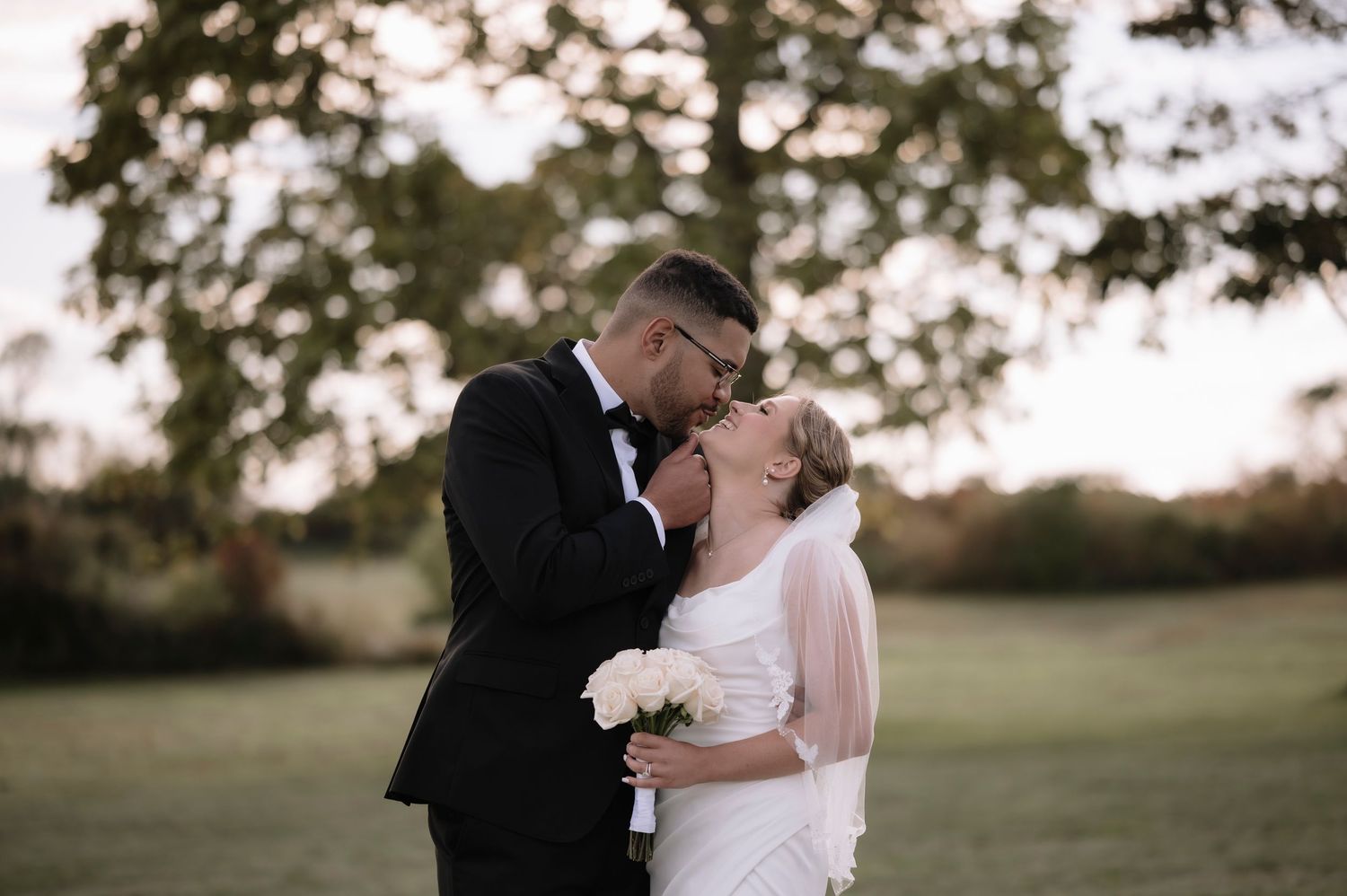 A romantic wedding couple shares an intimate moment in a sunlit outdoor field during golden hour.