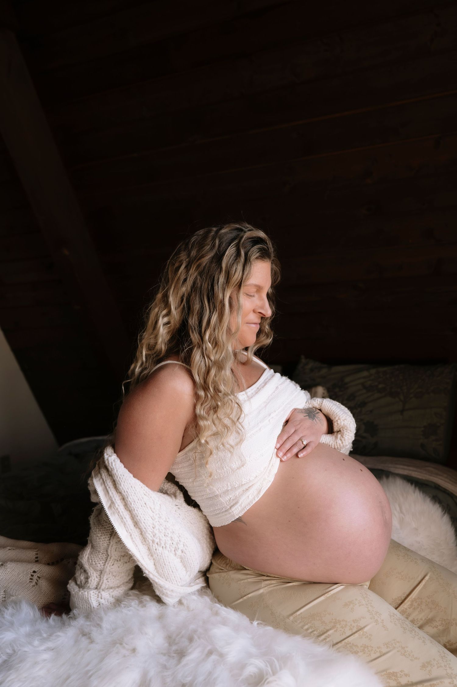 A maternity photo series showing someone in white lace lounging on cream bedding.