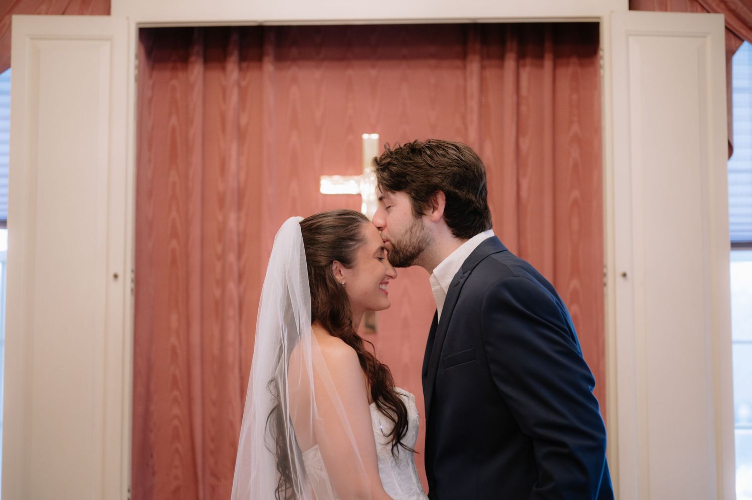 Romantic wedding portrait against coral colored door with white cross.
