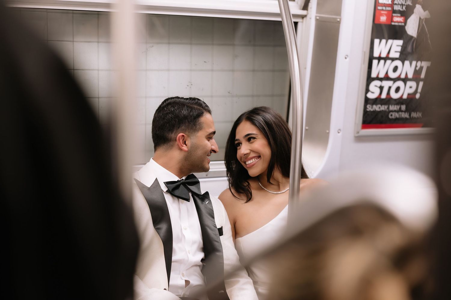 Happy couple in wedding attire sharing a candid moment in a subway car.