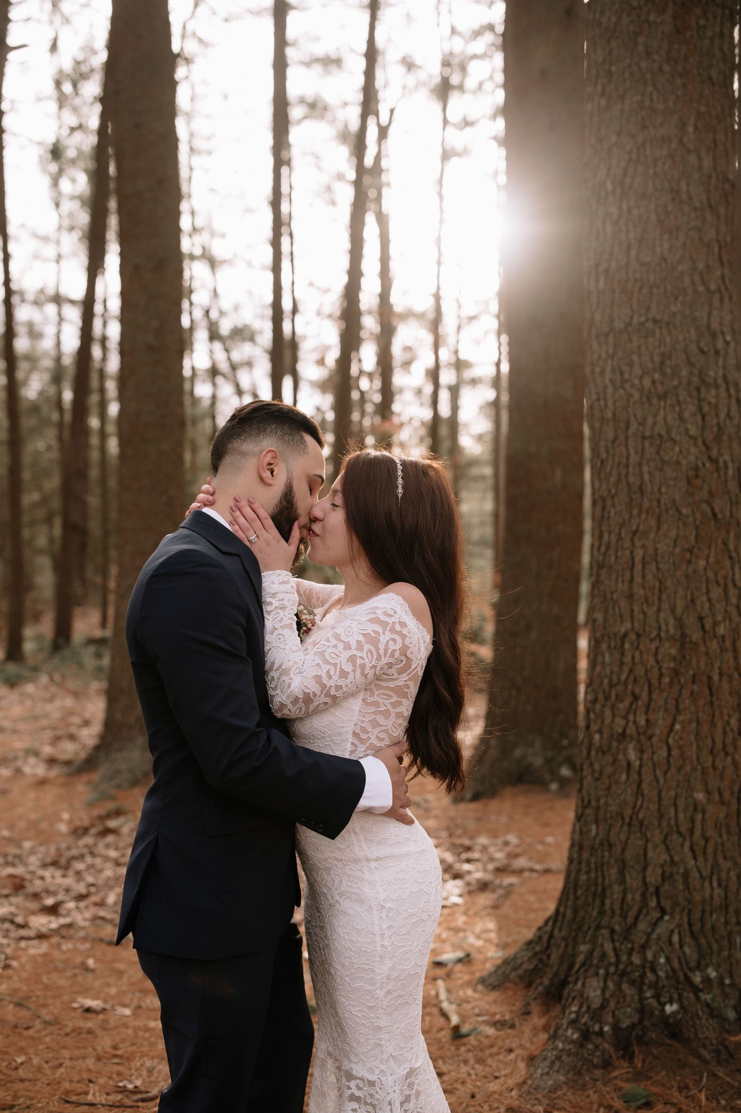 Couple in wedding attire sharing romantic moment in sunlit forest.