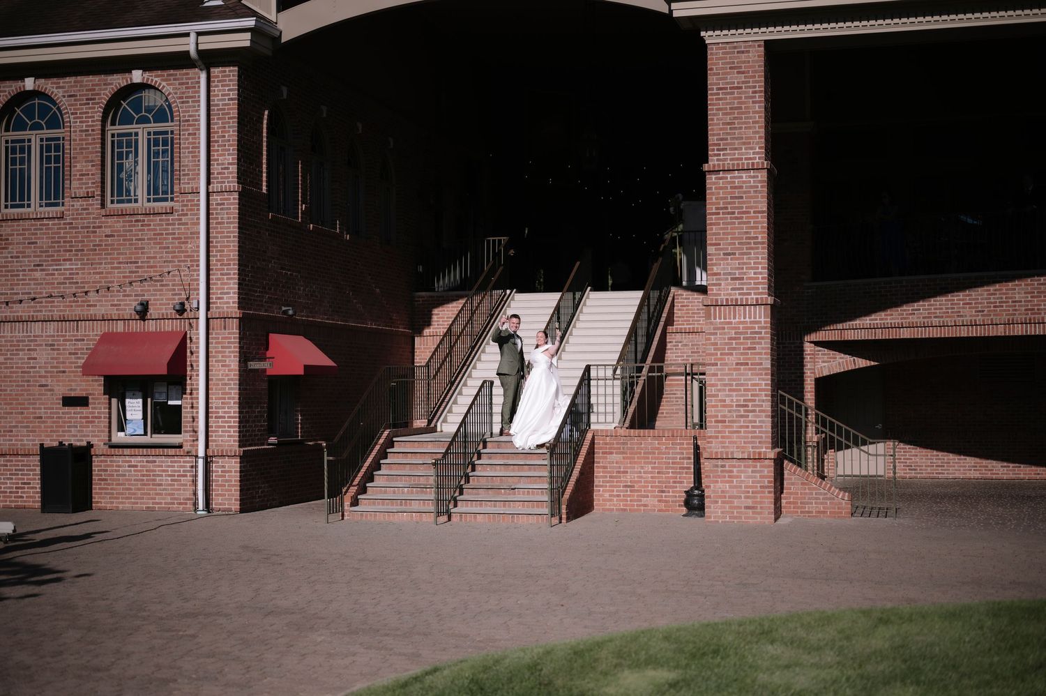 Brick building exterior with grand staircase entrance, red awnings, and a person standing on the steps in daylight.