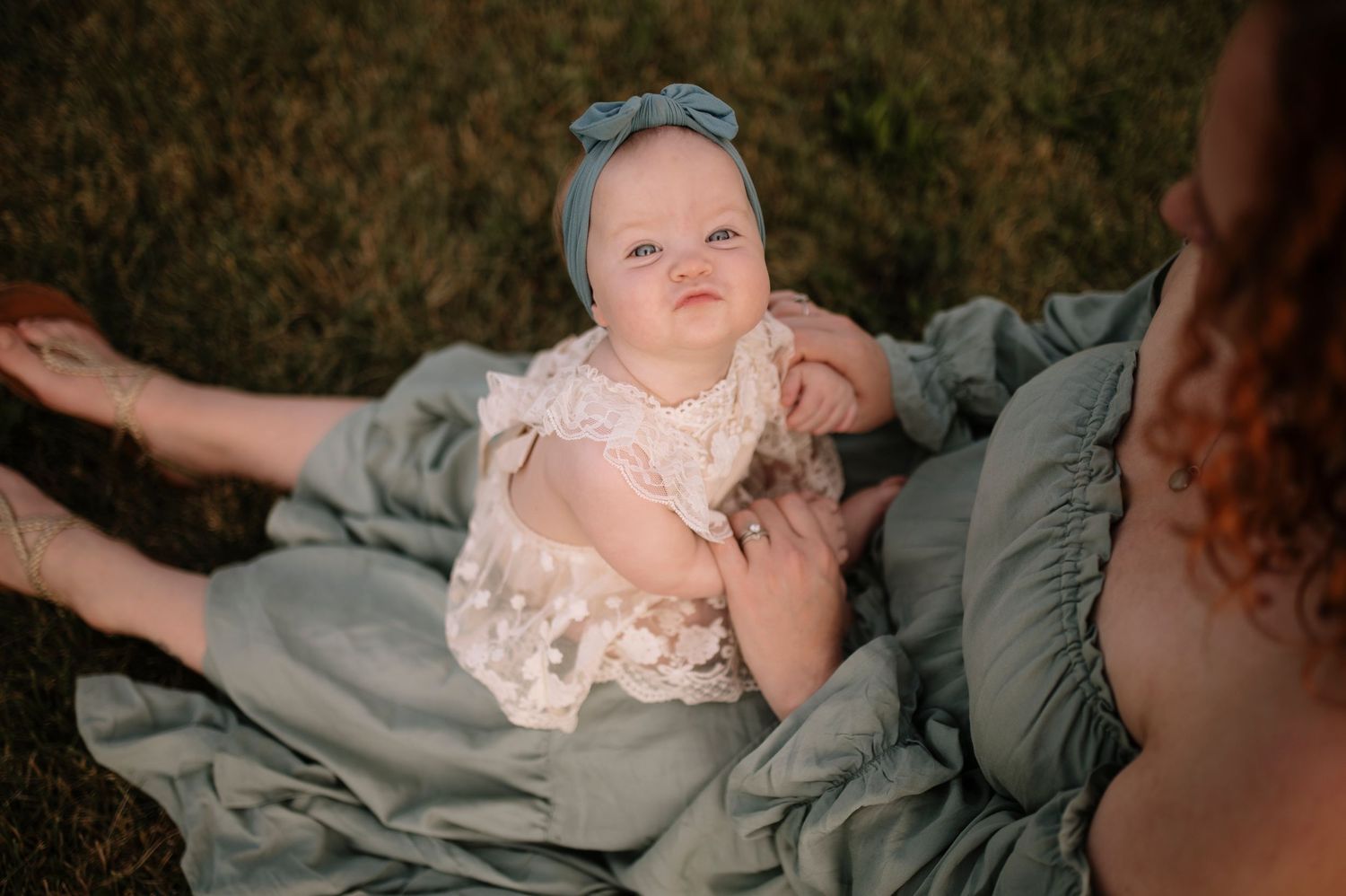 Baby wearing a delicate lace dress sits on a gray blanket during an outdoor photoshoot.