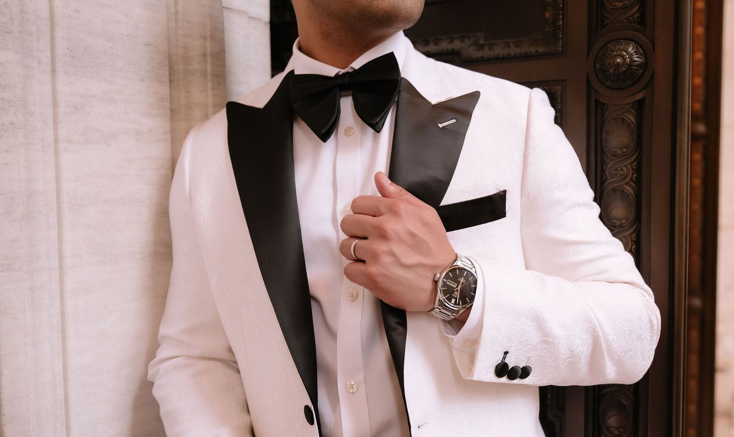 Elegant white tuxedo jacket with black lapels and bowtie, accented by a luxury watch on the wearer's wrist.