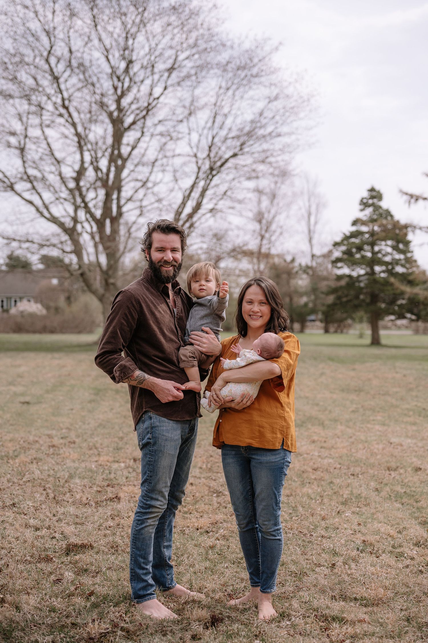 A family group stands together outdoors in casual clothing during fall.